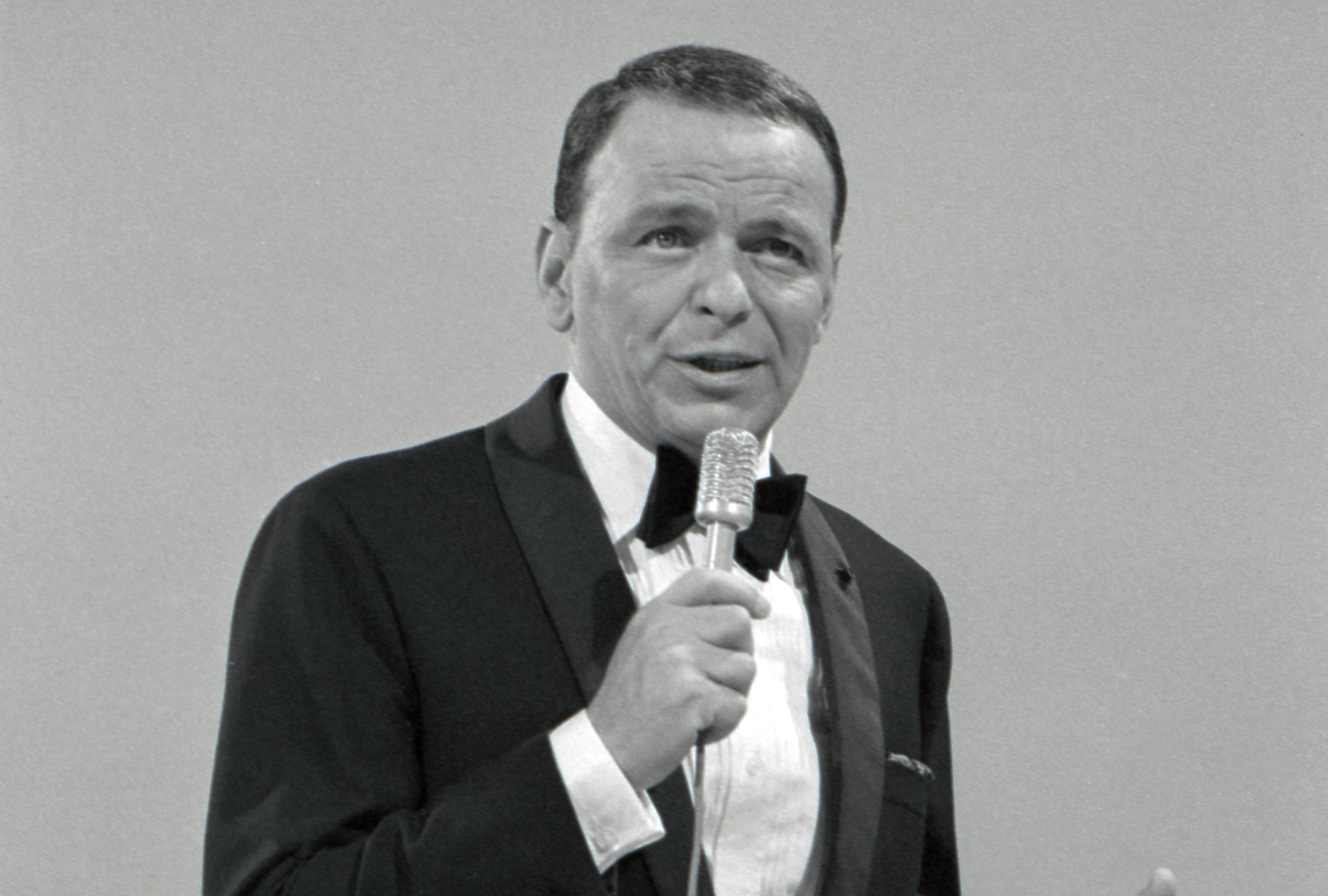 A black and white picture of Frank Sinatra wearing a tuxedo and holding a microphone.