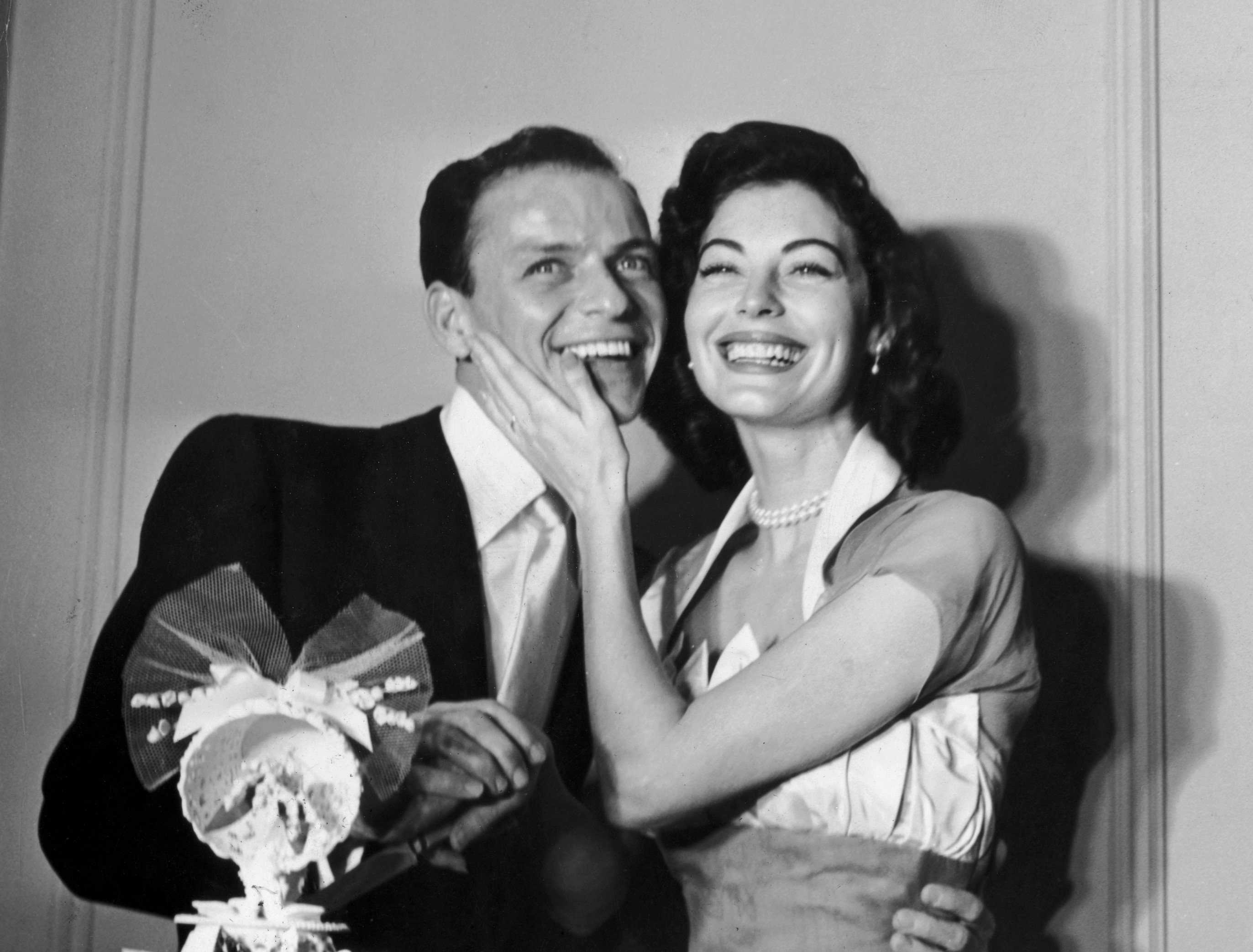 A black and white photo of Frank Sinatra and Ava Gardner on their wedding day. Gardner holds her hand to Sinatra's face.
