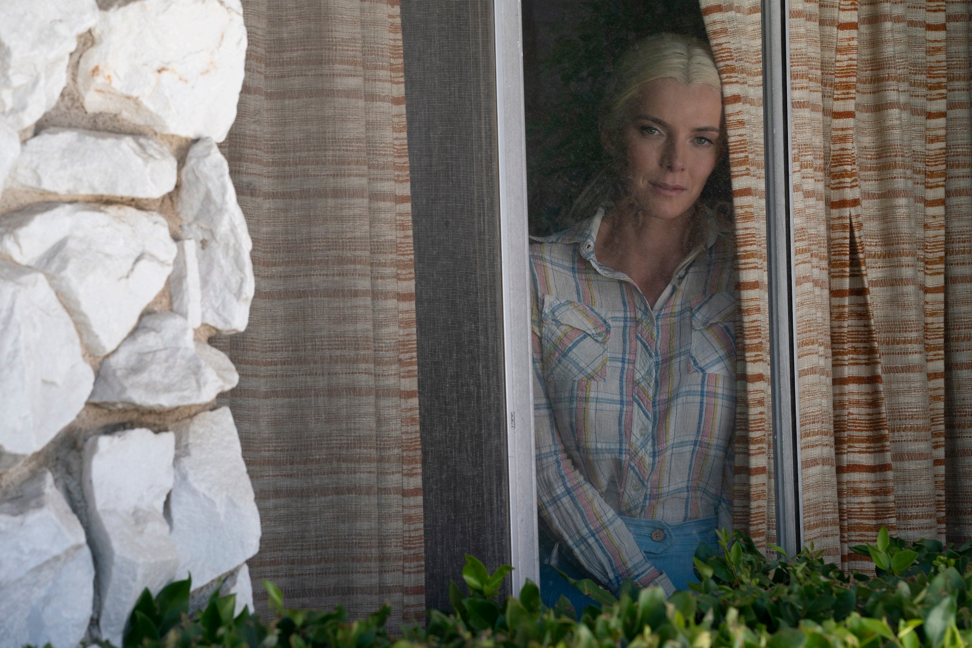 'Gaslit' Episode 4 'Malum in Se' production still featuring Betty Gilpin as Mo Dean wearing a plaid button down shirt while looking out a window.