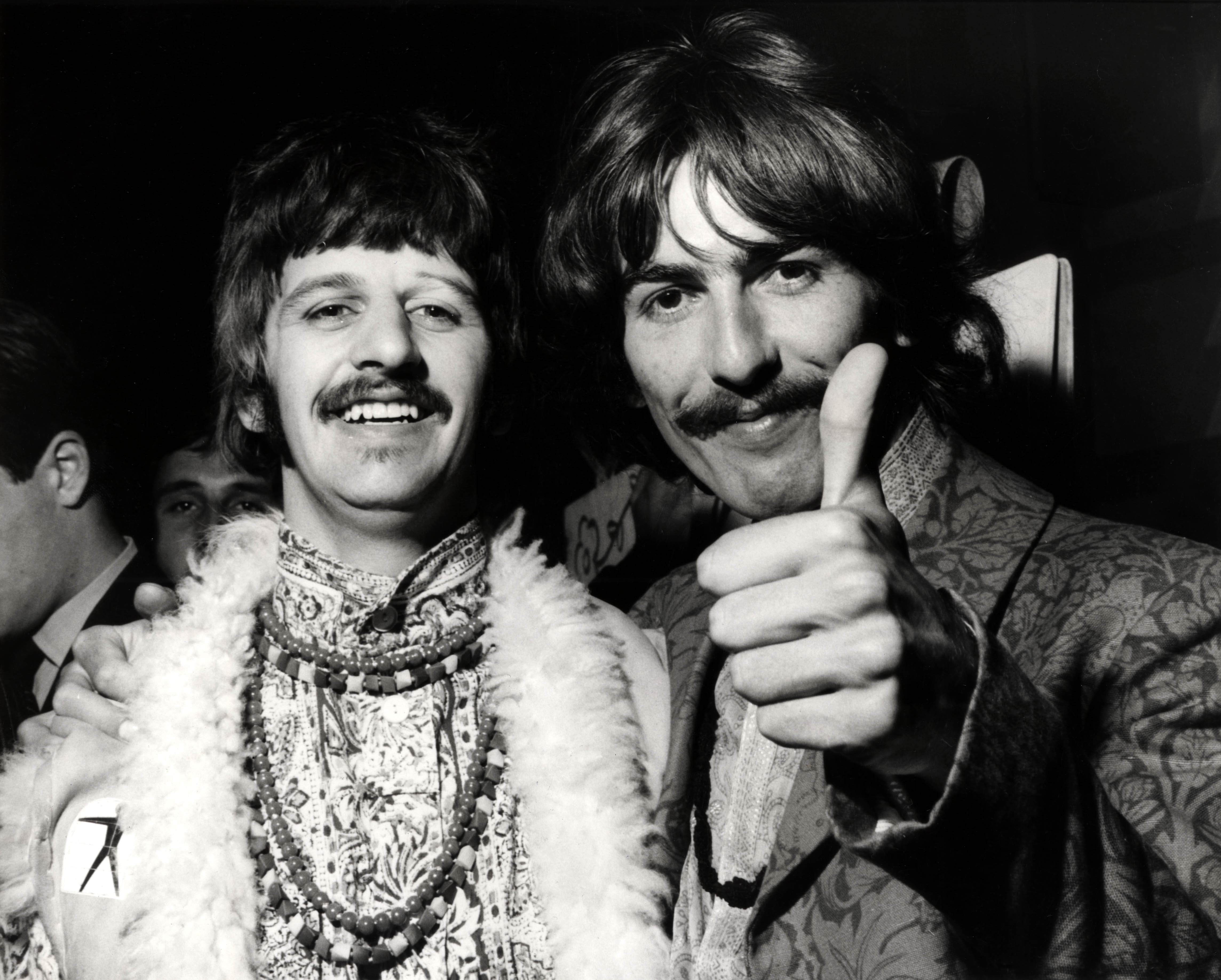 The Beatles' Ringo Starr standing next to George Harrison while the latter gives a thumbs up
