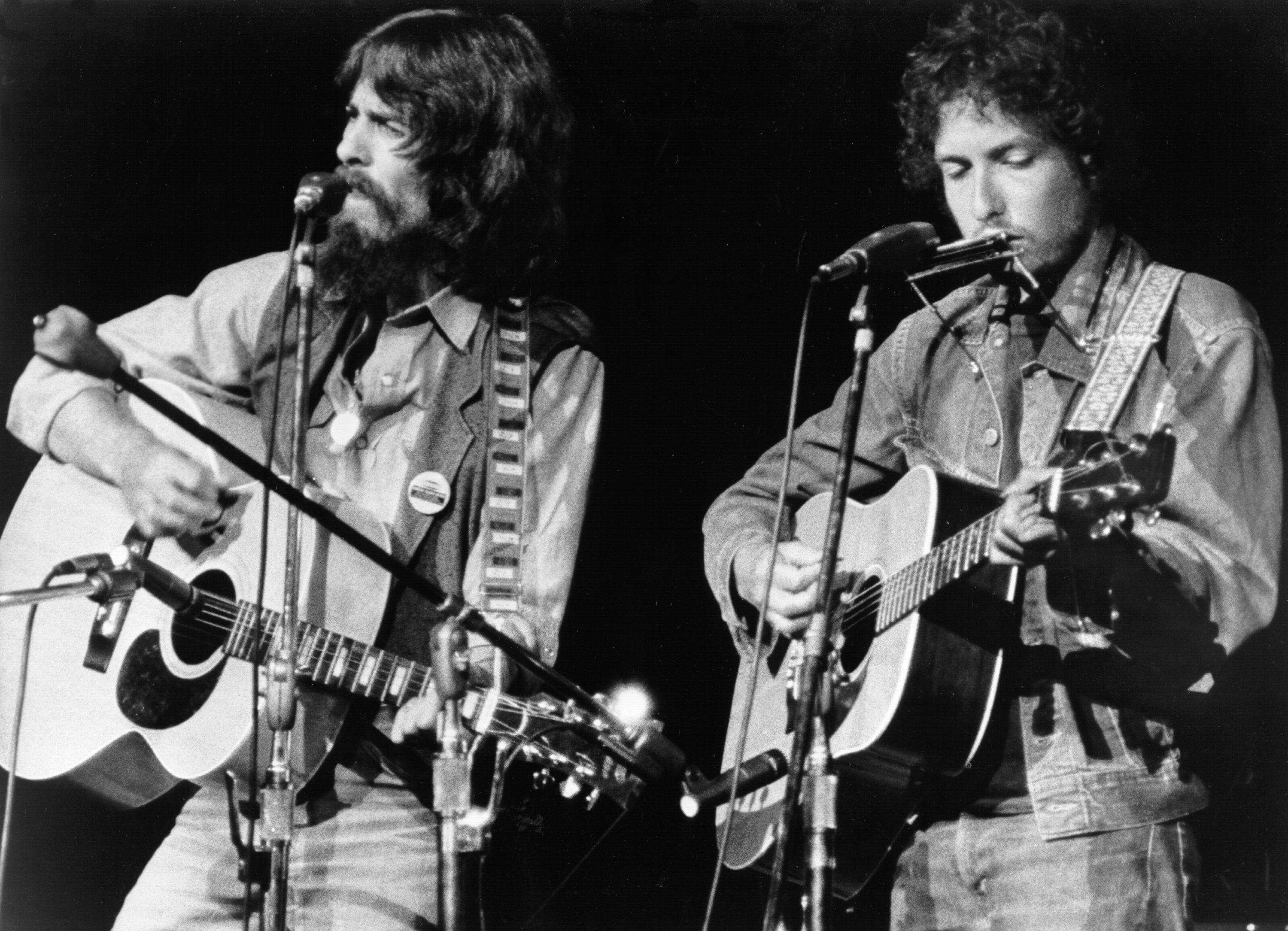 A black and white picture of George Harrison and Bob Dylan playing guitar and standing in front of microphones.