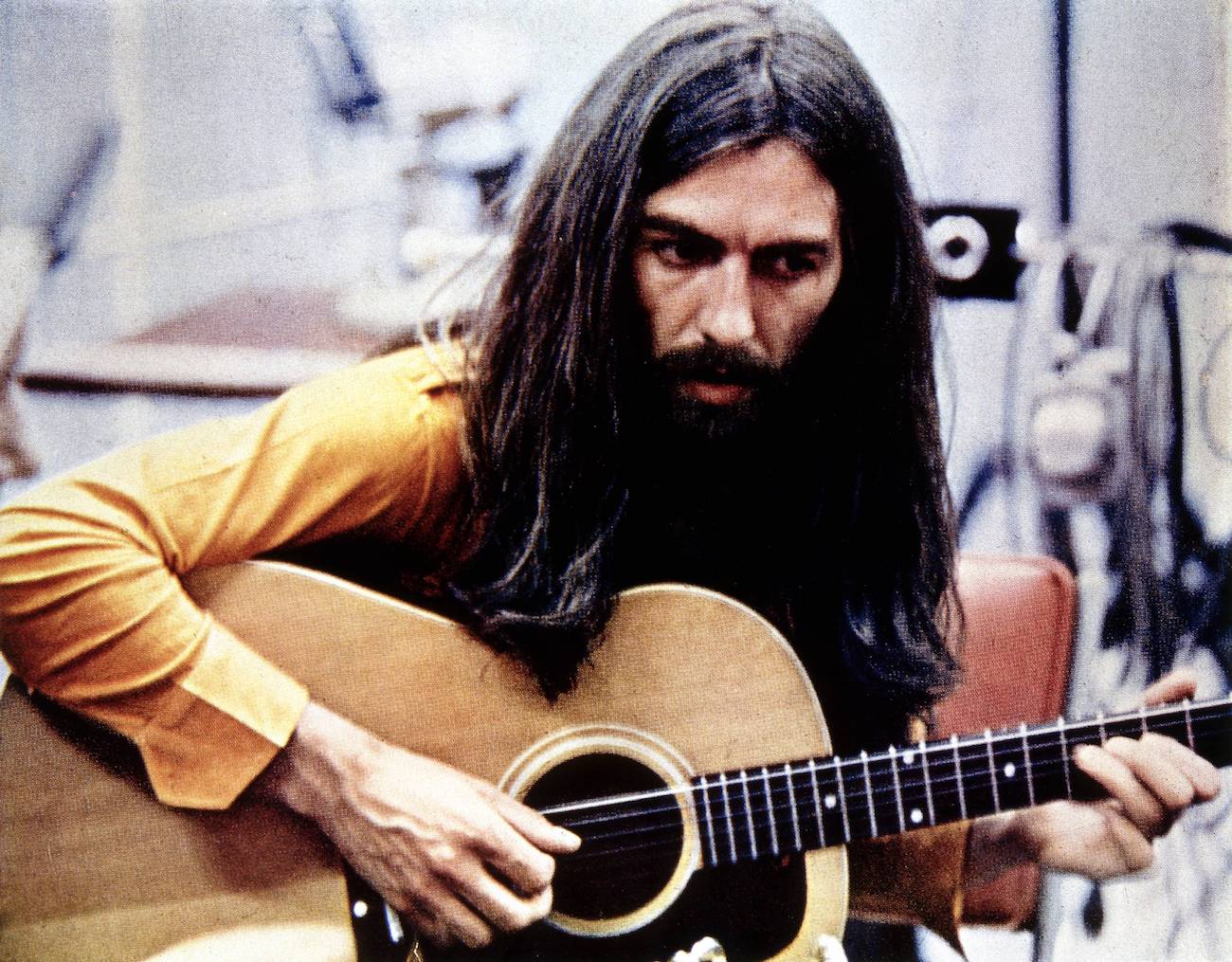 George Harrison in the recording studio wearing a yellow shirt and playing the guitar in 1970.