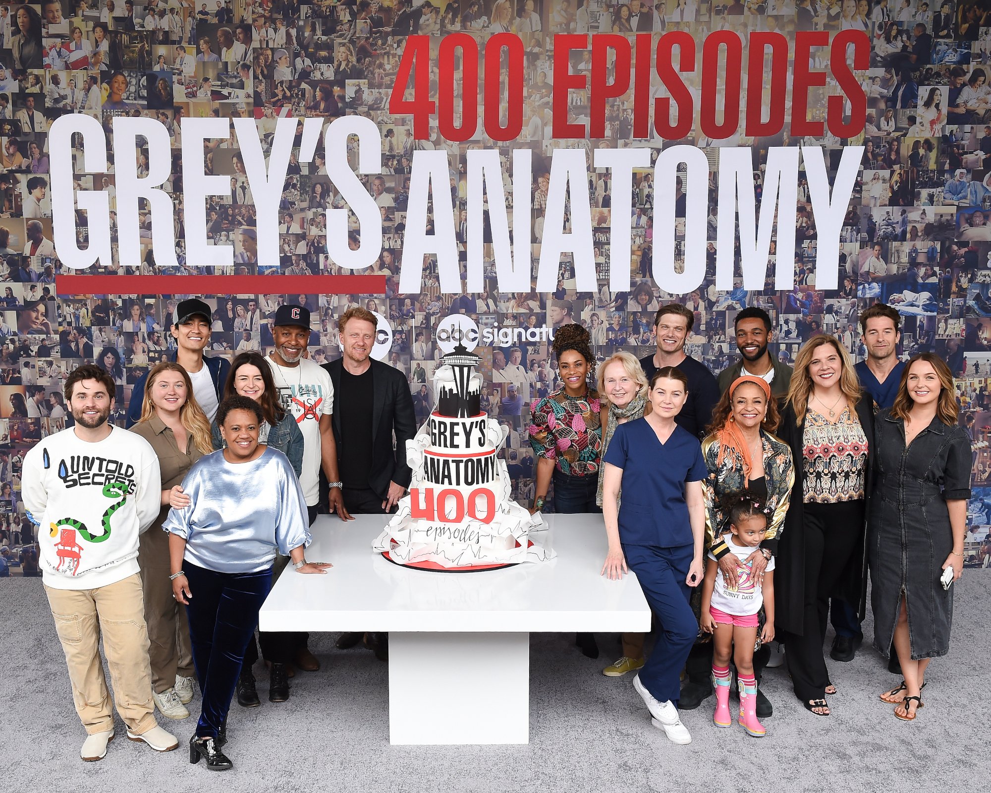 The 'Grey's Anatomy' cast, who discussed the possibility of the show ending at the 400-episode celebration. They're standing around a tall, white cake with 'Grey's Anatomy 400' on the front. They're also standing in front of a wall with pictures from the ABC series over the years.