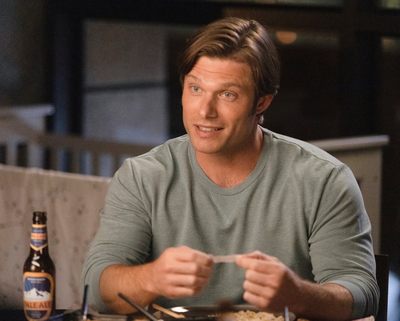 Chris Carmack as Link sits at a dinner table reading a fortune from a fortune cookie in 'Grey's Anatomy'.