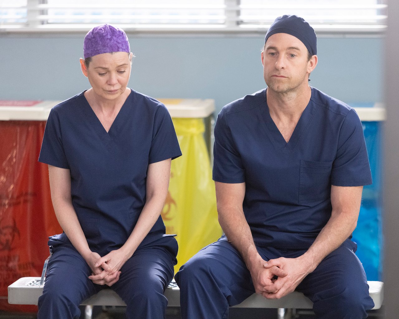 Ellen Pompeo as Meredith Grey and Scott Speedman as Nick Marsh sit next to each other in blue scrubs on 'Grey's Anatomy'.
