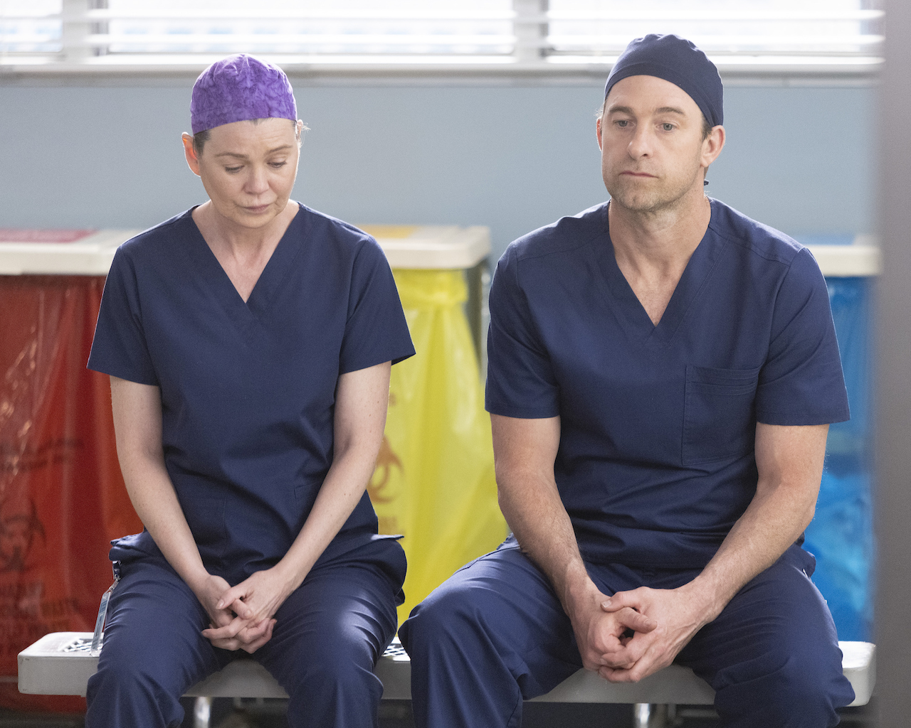 Ellen Pompeo as Meredith Grey and Scott Speedman as Nick Marsh sit next to each other in blue scrubs on 'Grey's Anatomy'.