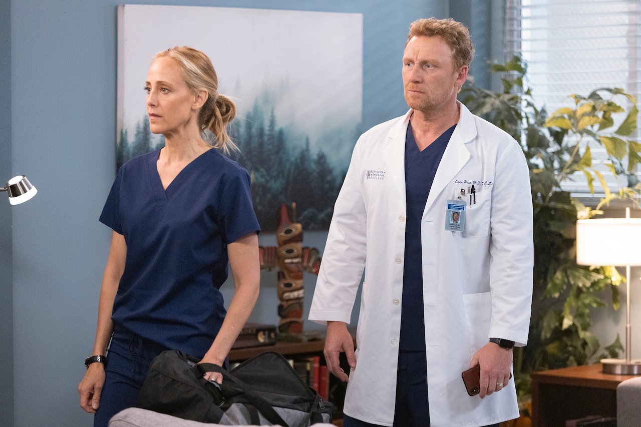 Kim Raver as Teddy Altman and Kevin McKidd as Owen Hunt stand next to each other looking worried in 'Grey's Anatomy'.