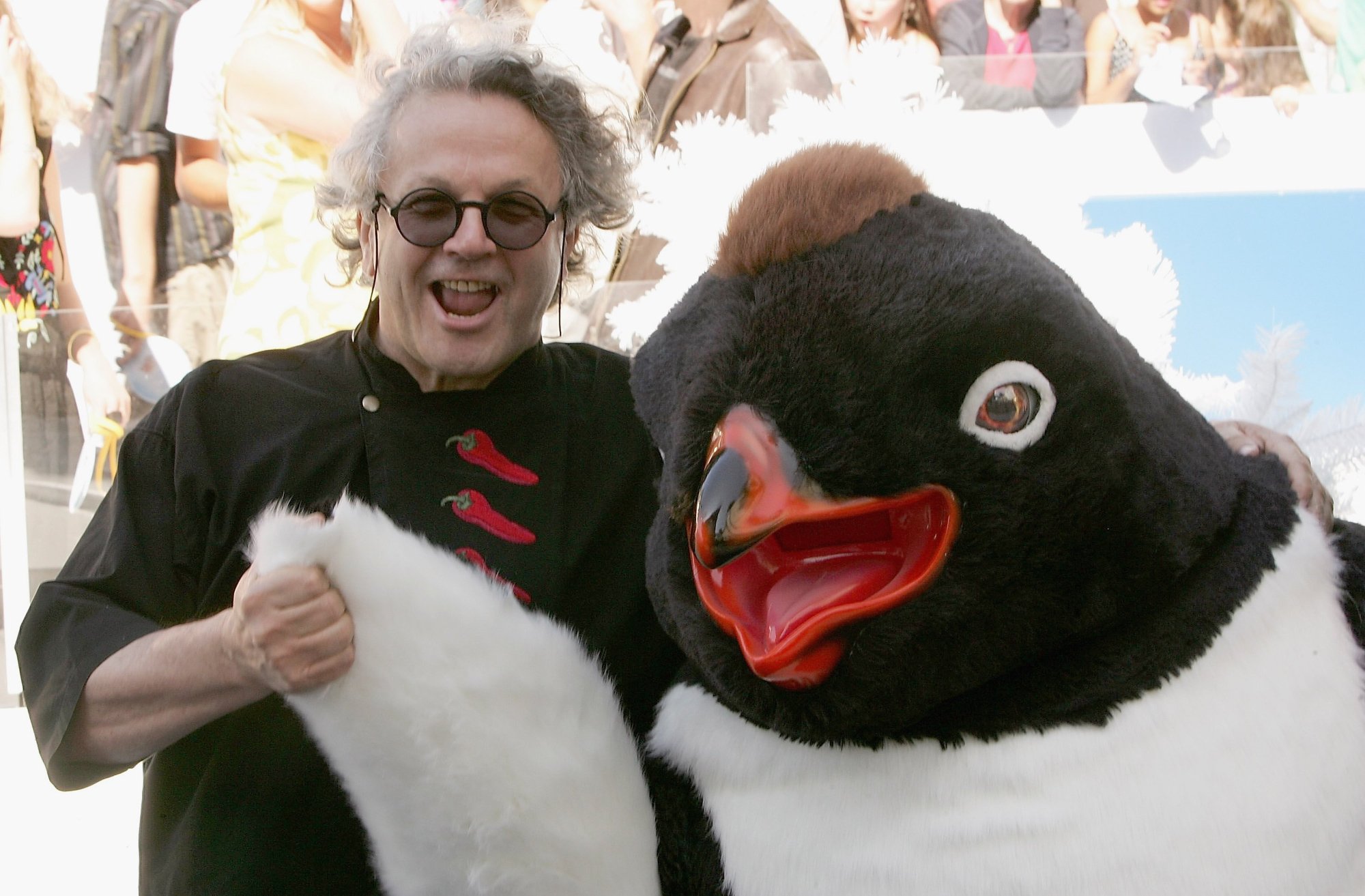 'Happy Feet' filmmaker George Miller wearing black and sunglasses, holding the flipper of a costumed penguin