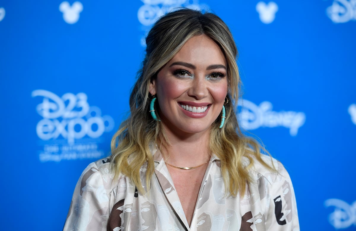 Hilary Duff stands in front of a Disney backdrop and smiles