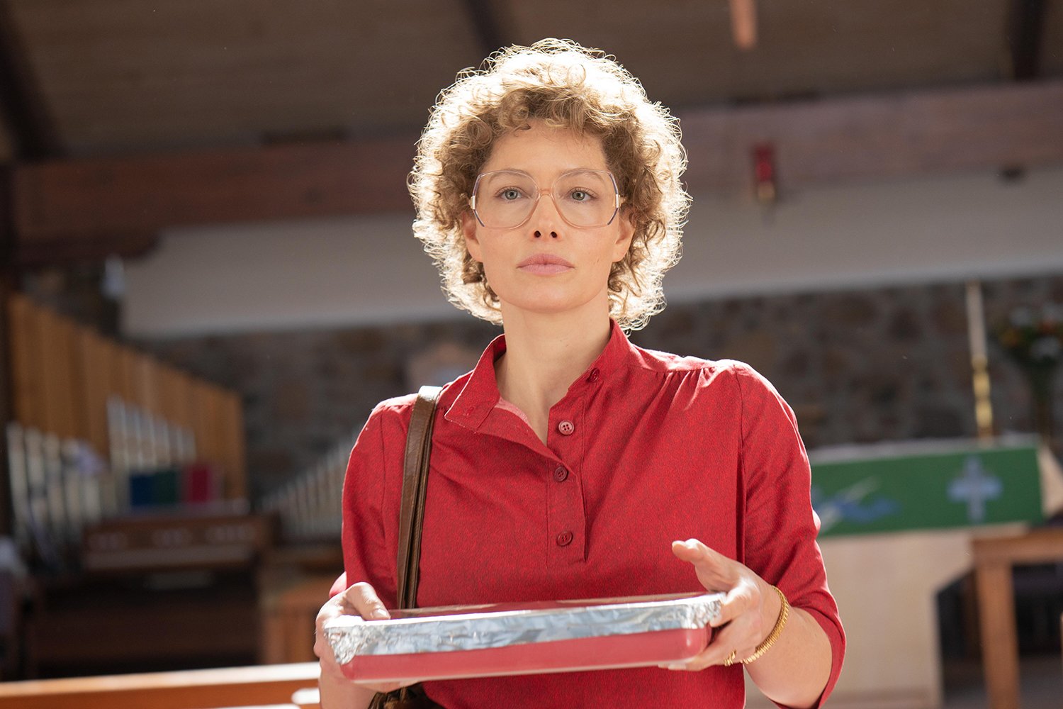 Jessica Biel wearing a red shirt and holding a dish in a production still of Hulu's Candy.