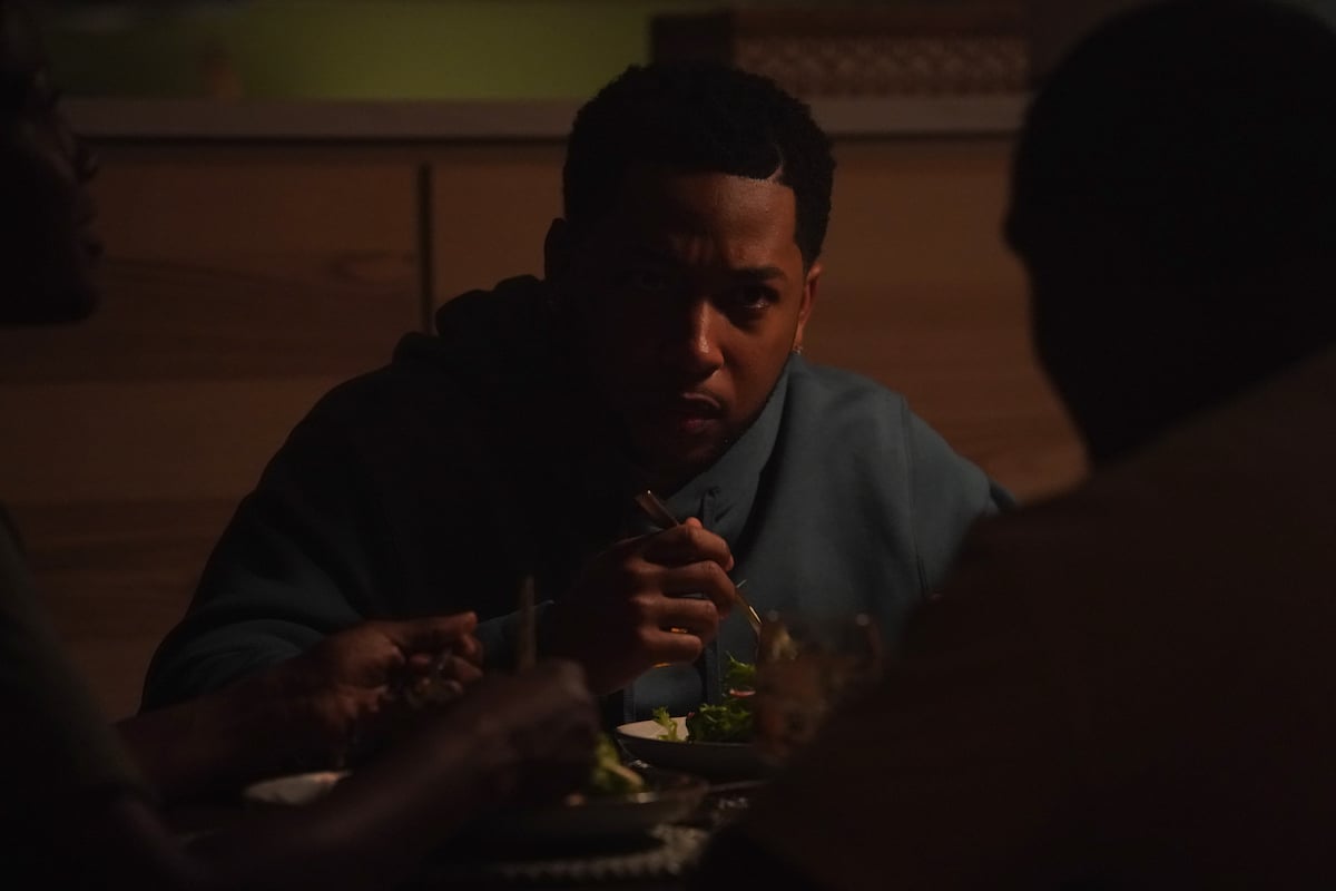 Jacob Latimore of 'The Chi' Season 5 appears in a scene as his character Emmett. He has on a blue hooded sweatshirt while talking at dinner.