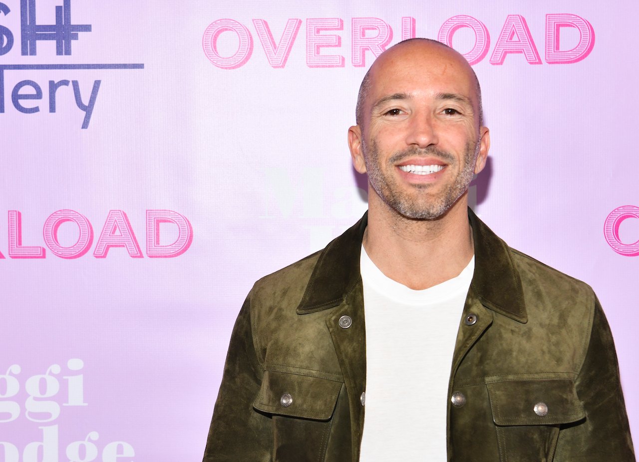 Jason Oppenheim poses in a white shirt and denim jacket on the red carpet.