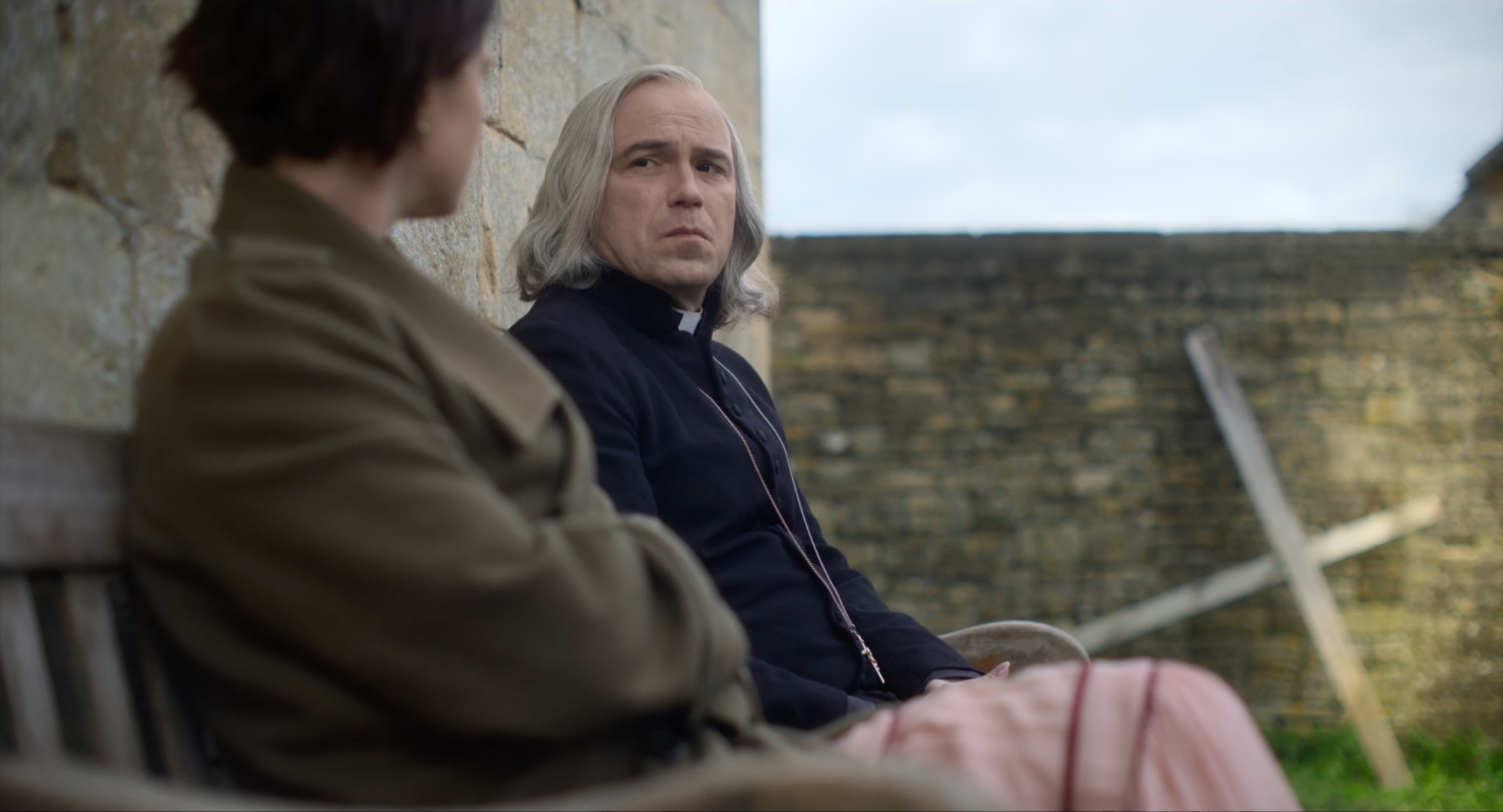 Jessie Buckley as Harper and Rory Kinnear as the priest in 'Men' sitting on a bench looking at each other