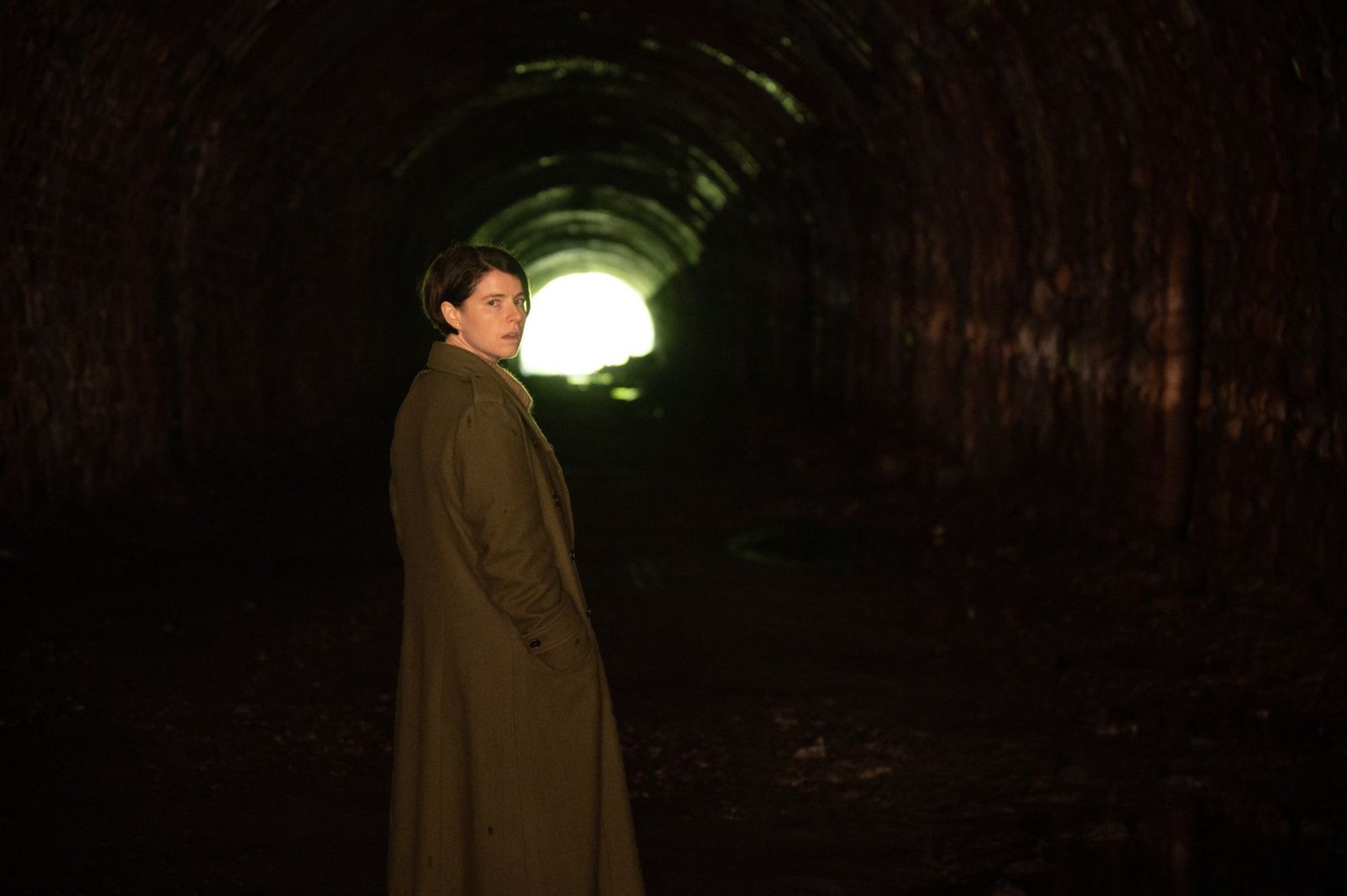 Jessie Buckley as Harper in 'Men', an A24 film about toxic masculinity standing in a tunnel looking over her shoulder