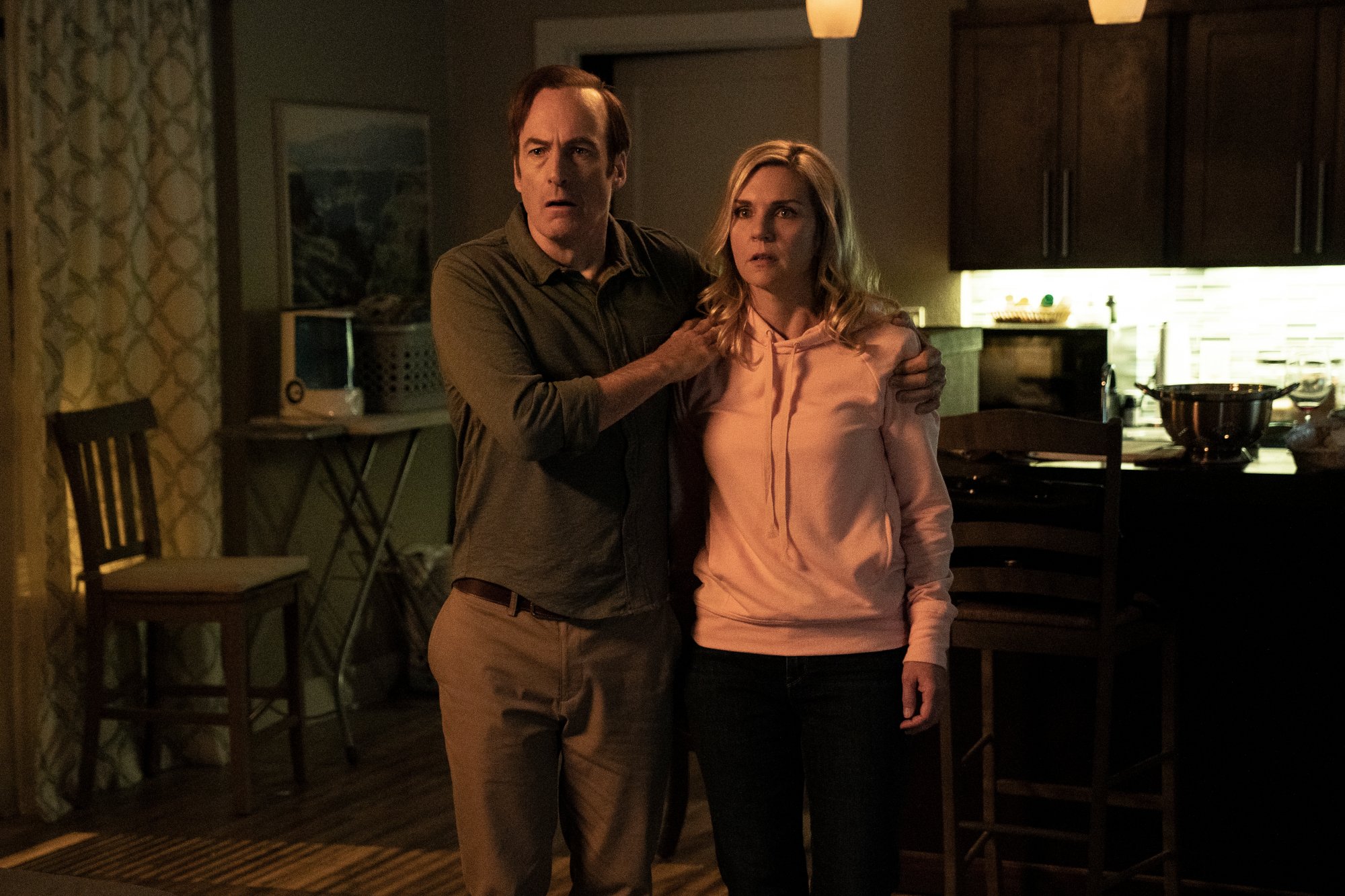 Bob Odenkirk and Rhea Seehorn as Saul Goodman and Kim Wexler in 'Better Call Saul' Season 6 Part 1, which left off on a shocking note heading into part 2. He's wearing a brown shirt and brown pants, and she's wearing a pink sweatshirt. He's holding onto her shoulders, and both characters look scared.
