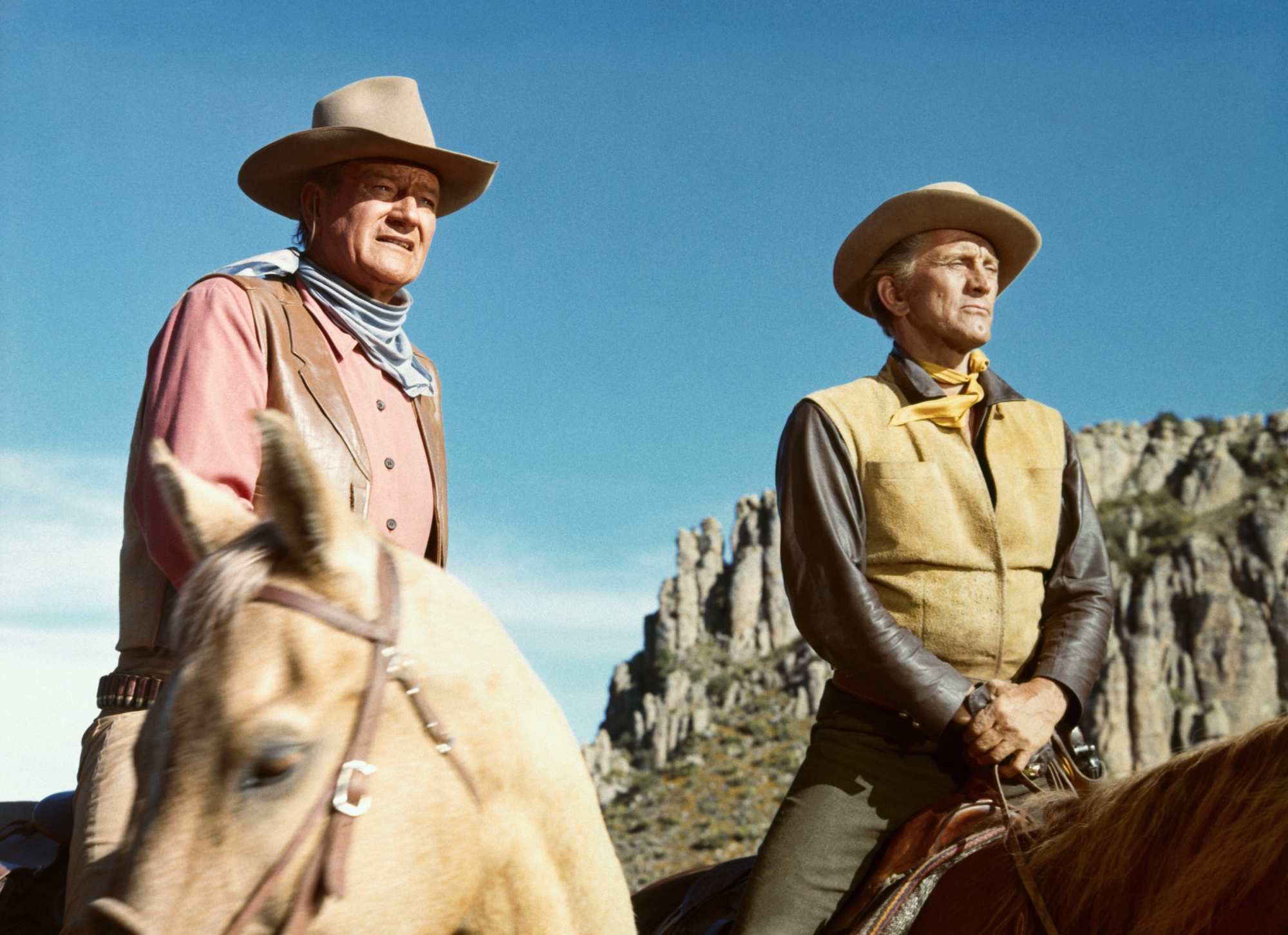 John Wayne as Taw Jackson and Kirk Douglas as Lomax in 'The War Wagon' sitting on horseback in cowboy uniforms