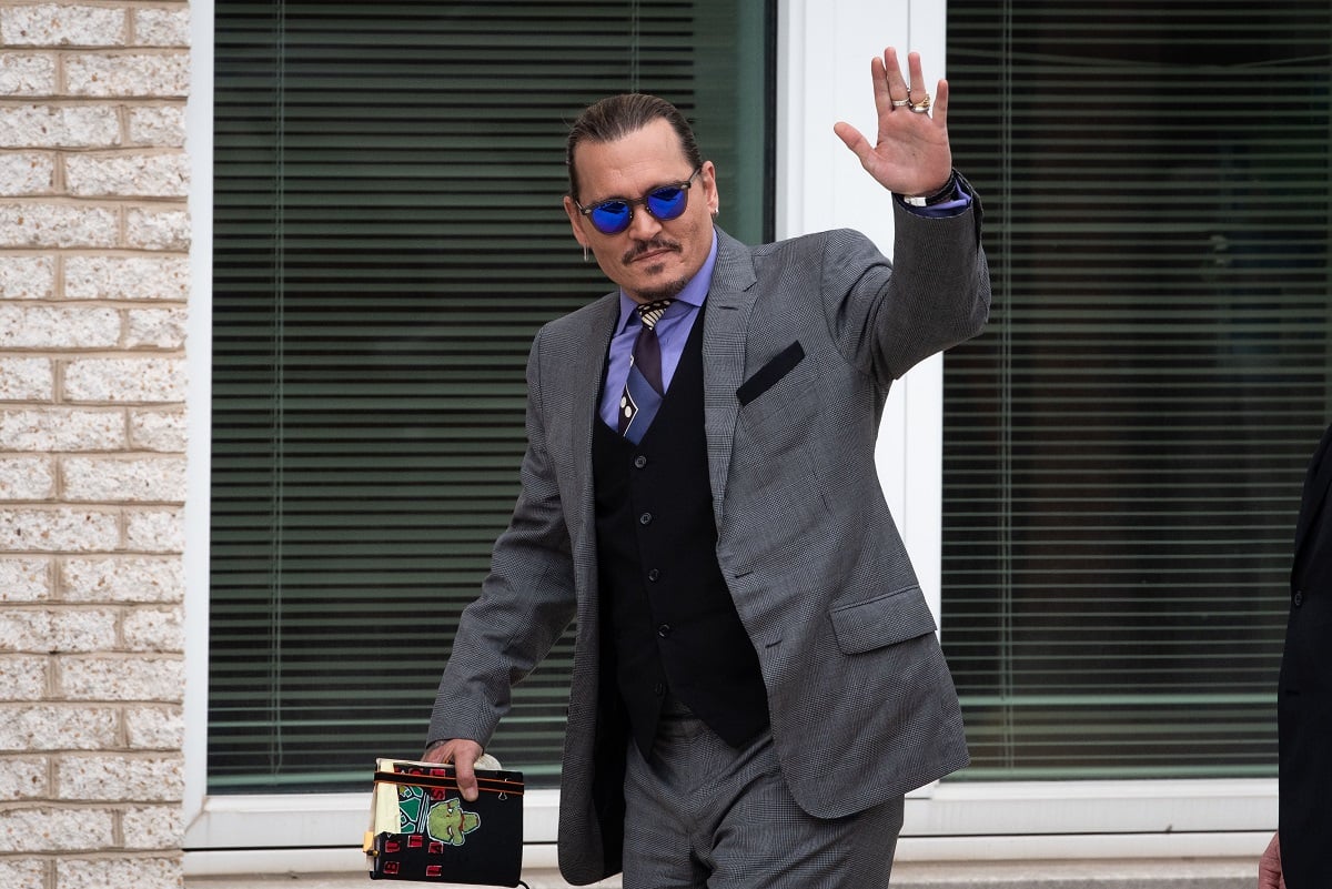 Johnny Depp waving at the camera in a grey suit.