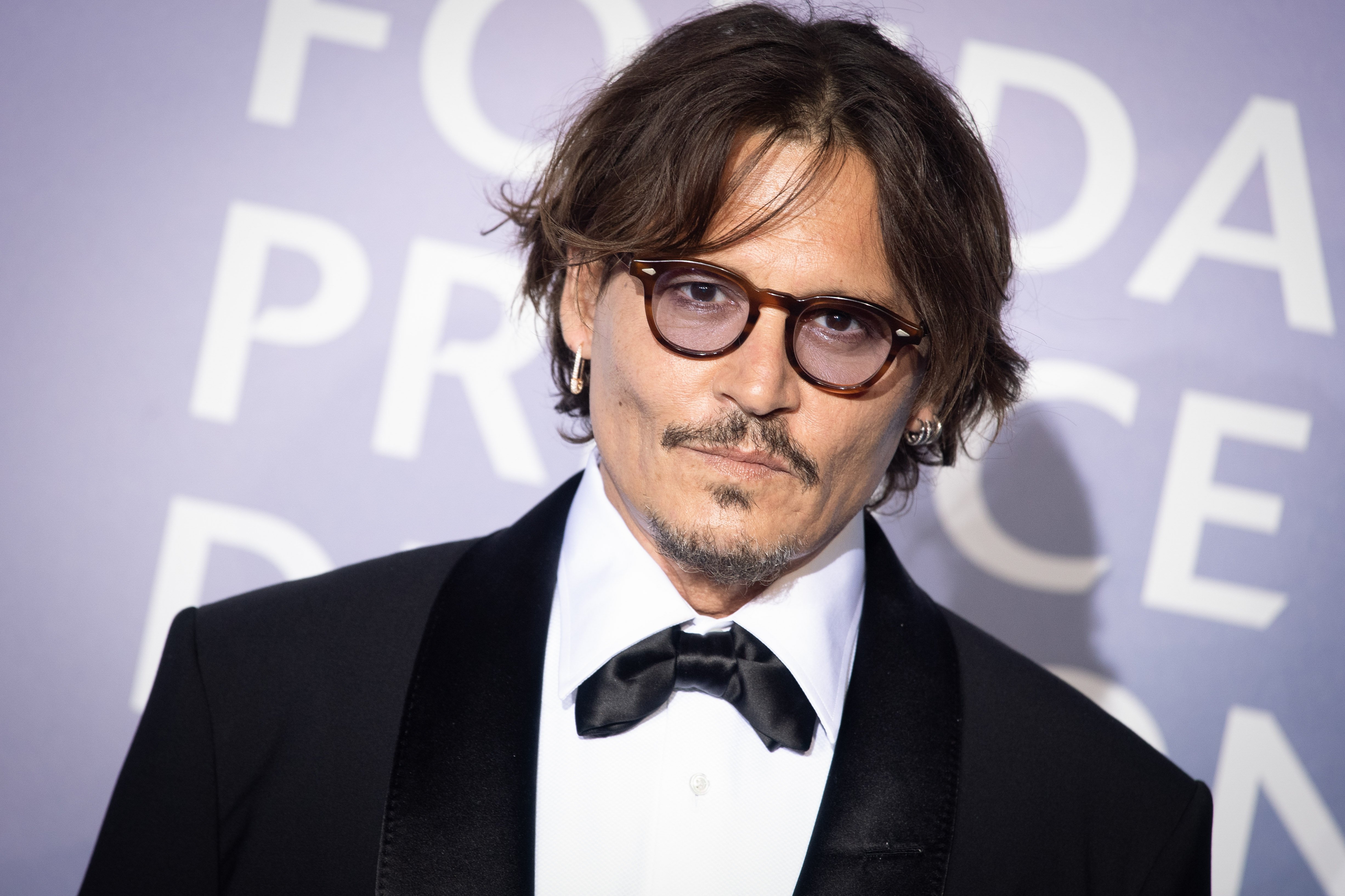 Johnny Depp poses at an event while wearing a black suit and white shirt.