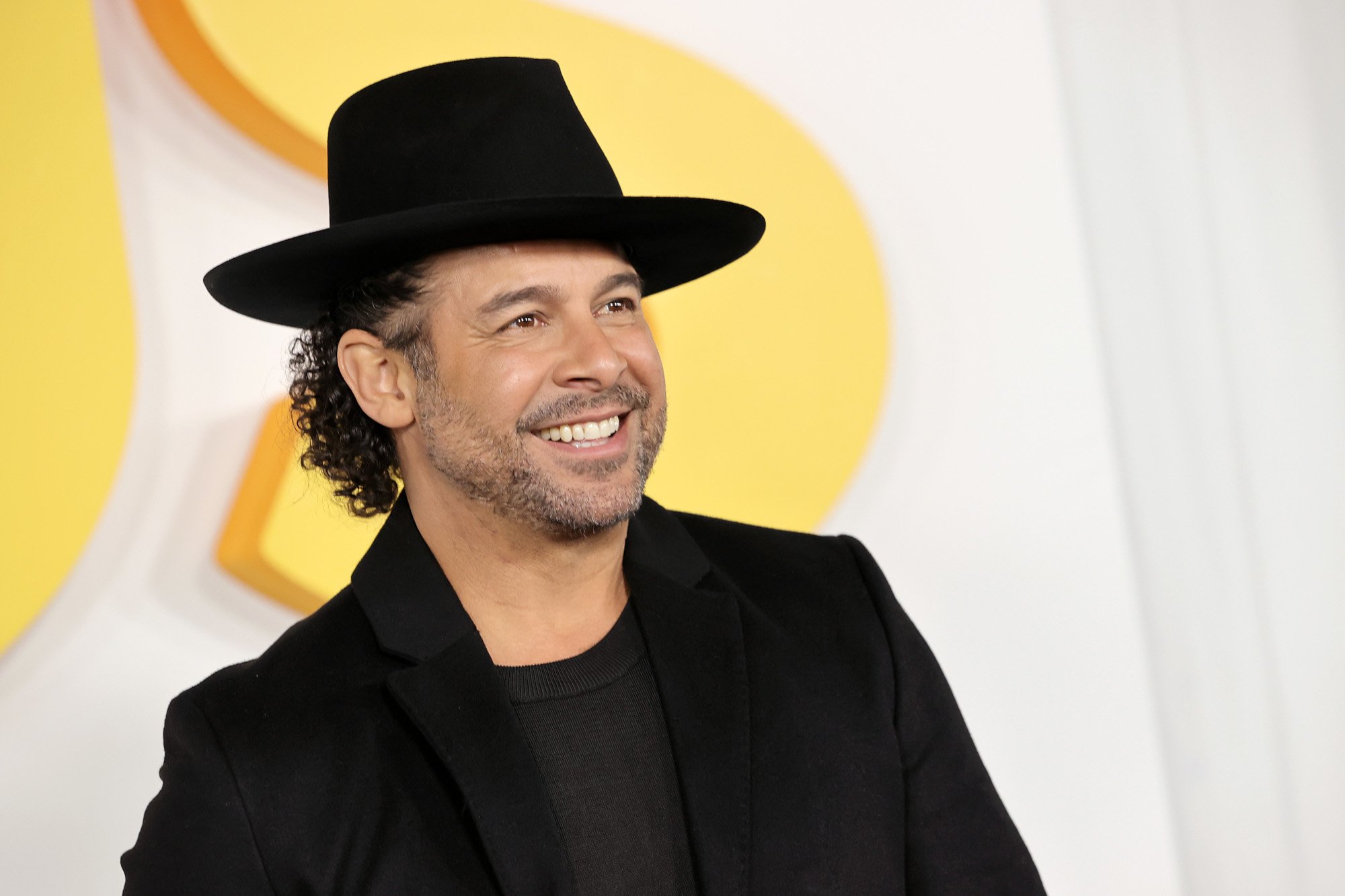 Miguel Rivas actor Jon Huertas at the premiere for 'This Is Us' Season 6. He's wearing a black shirt, black jacket, and black hat.