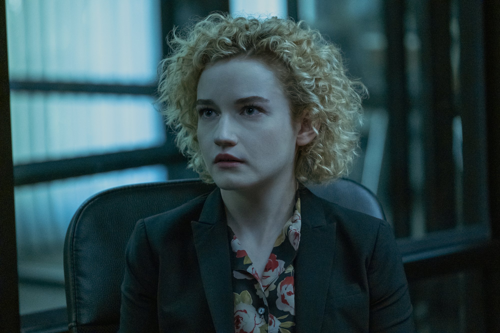 Julia Garner as Ruth Langmore in 'Ozark' Season 3 Episode 5. She's sitting in a desk chair and wearing a black blazer and floral shirt.