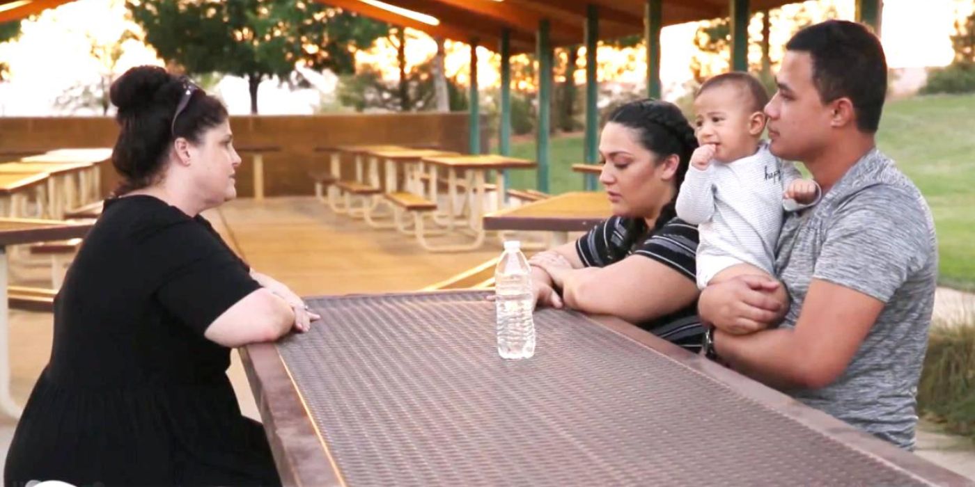 Lisa Faagata sits across from Kalani Faagata and Asuelu Pulaa holding a baby, sitting at a picnic table at a park on '90 Day Fiancé.