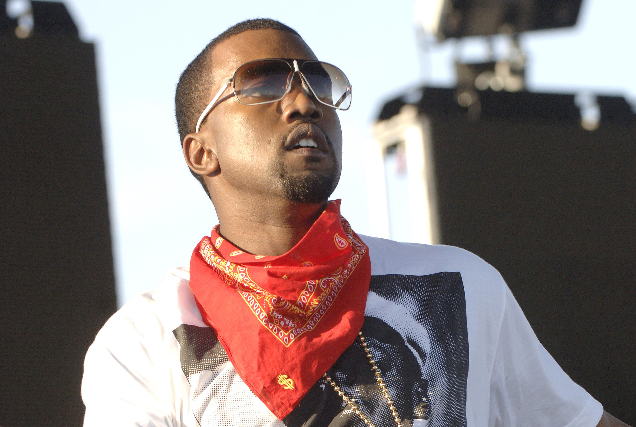 A close-up of Kanye West wearing sunglasses and a red bandana around his neck