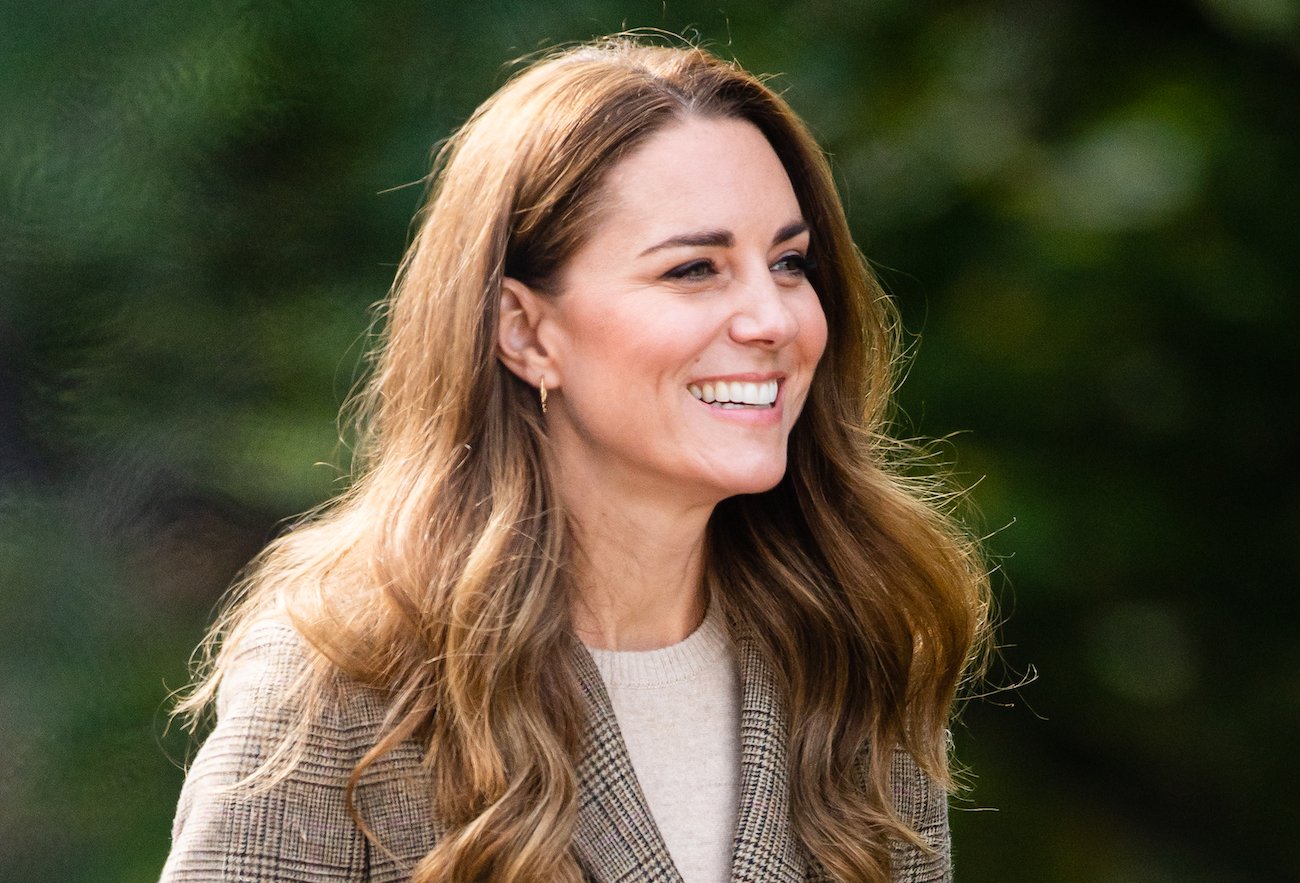 Kate Middleton wearing a plaid jacket and looking toward the left side of the photo
