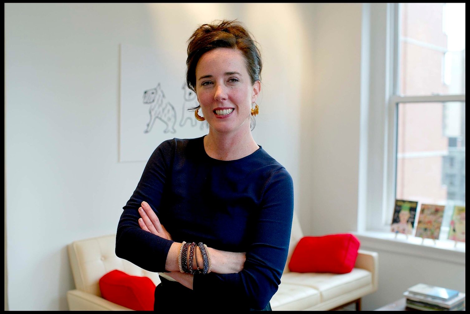 Designer Kate Spade smiling with her arms folded across her chest. Kate Spade's net worth is $200 million.