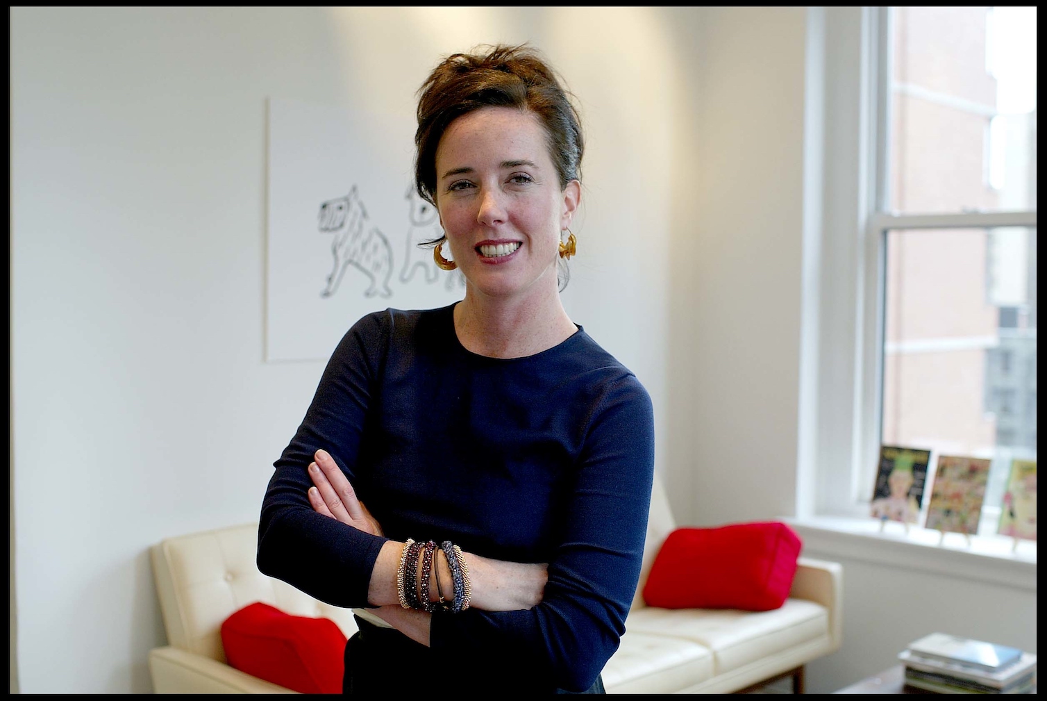Designer Kate Spade smiling with her arms folded across her chest. Kate Spade's net worth is $200 million.