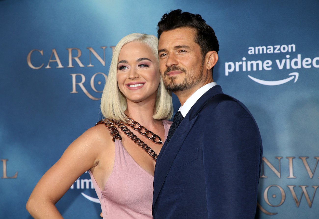 Katy Perry wearing a light pink outfit and standing next to Orlando Bloom, who is wearing a dark outfit