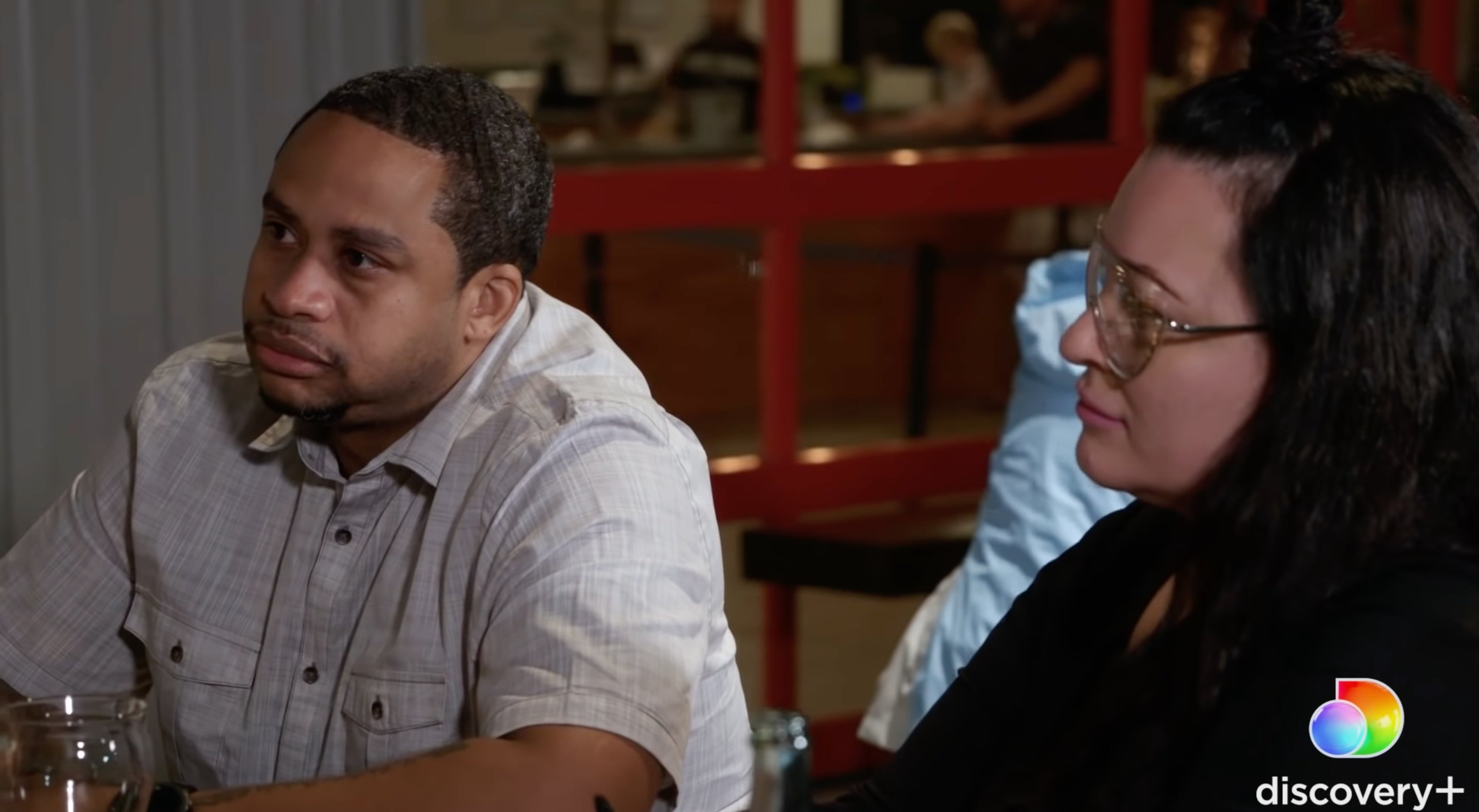 Kelly Brown wearing a grey polo shirt, sitting next to his girlfriend, Molly Hopkins in a restaurant in Georgia on '90 Day: The Single Life' Season 2.