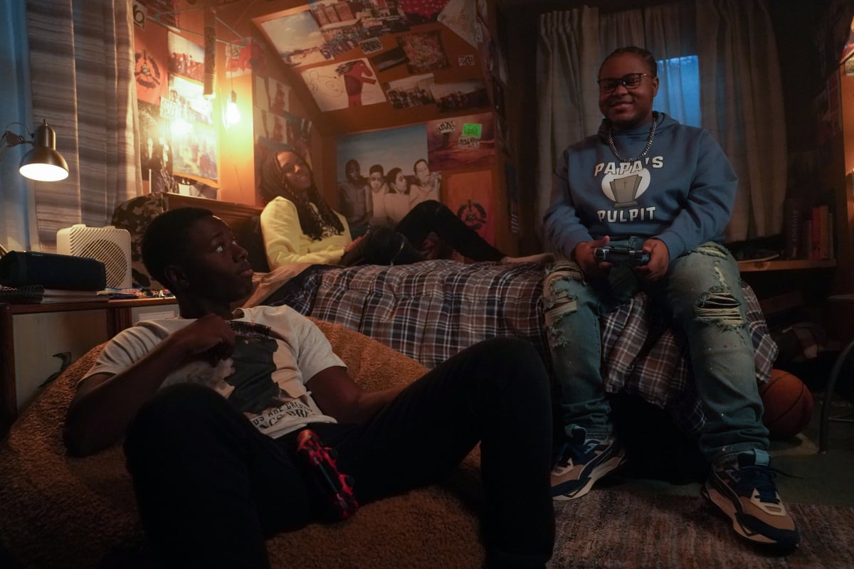 A scene of Kevin, Jake, and Papa in a scene from 'The Chi' Season 5. Kevin and Papa play a video together as Jake kicks back on a bed.