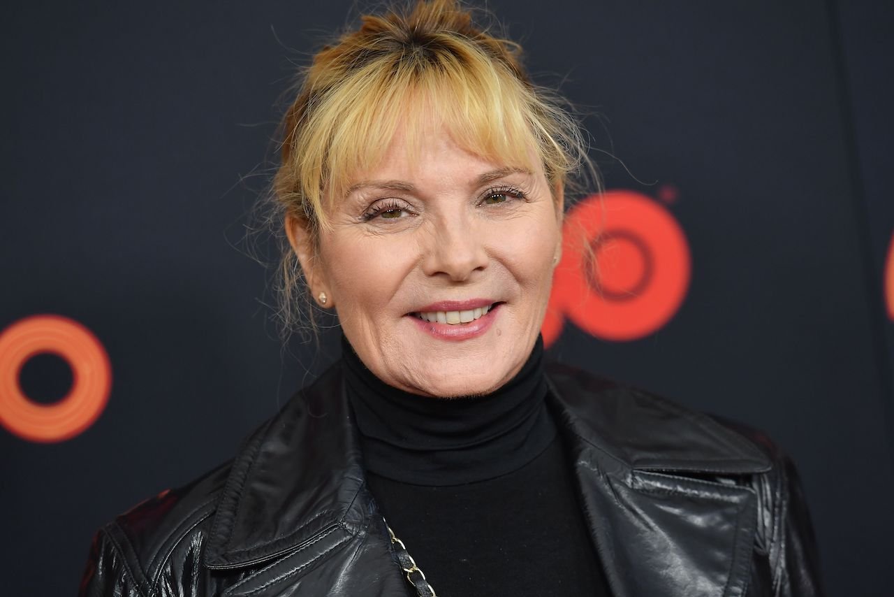 Kim Cattrall poses in a black outfit smiling on the red carpet.