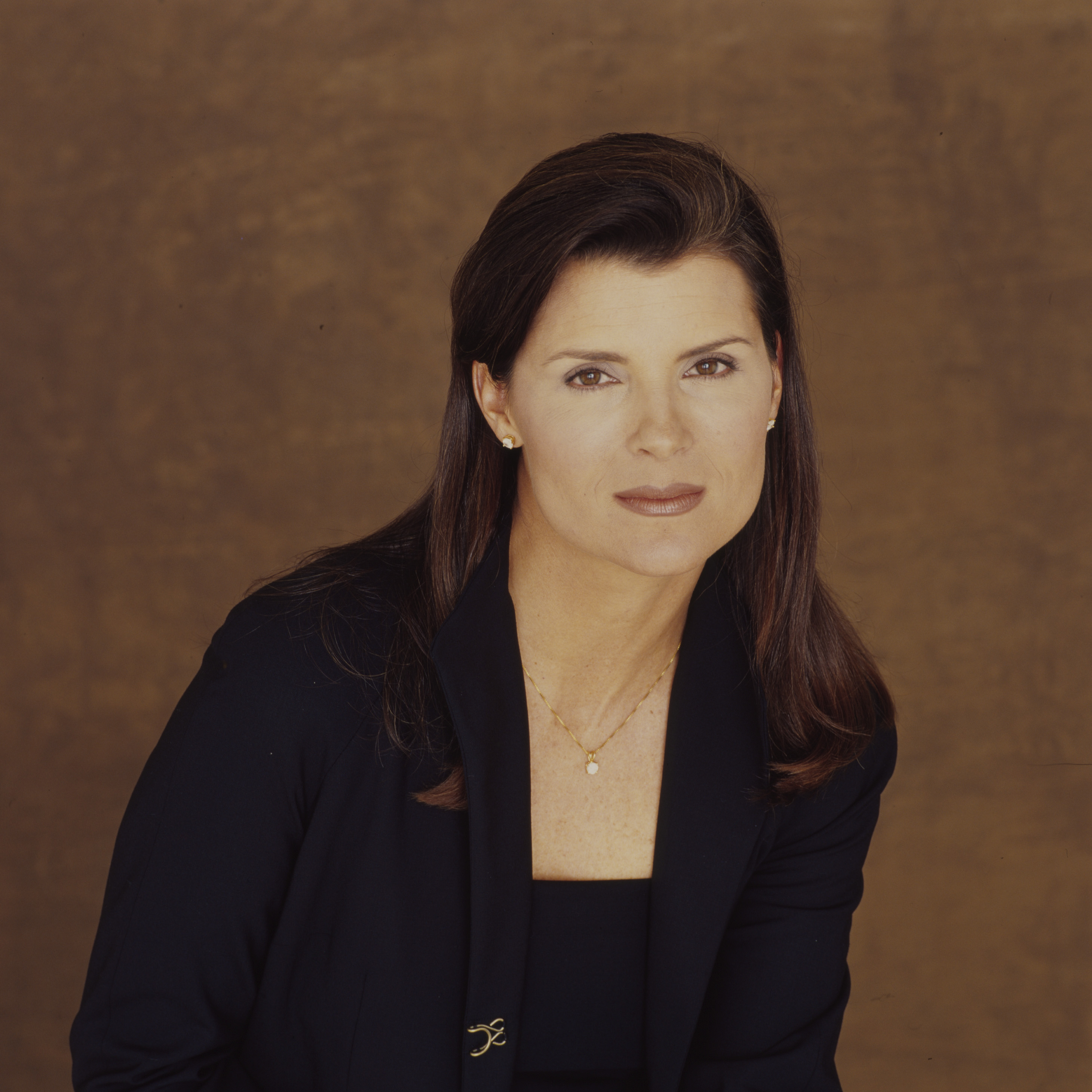 'The Bold and the Beautiful' star Kimberlin Brown wearing a navy blue suit and standing in front of a brown backdrop.