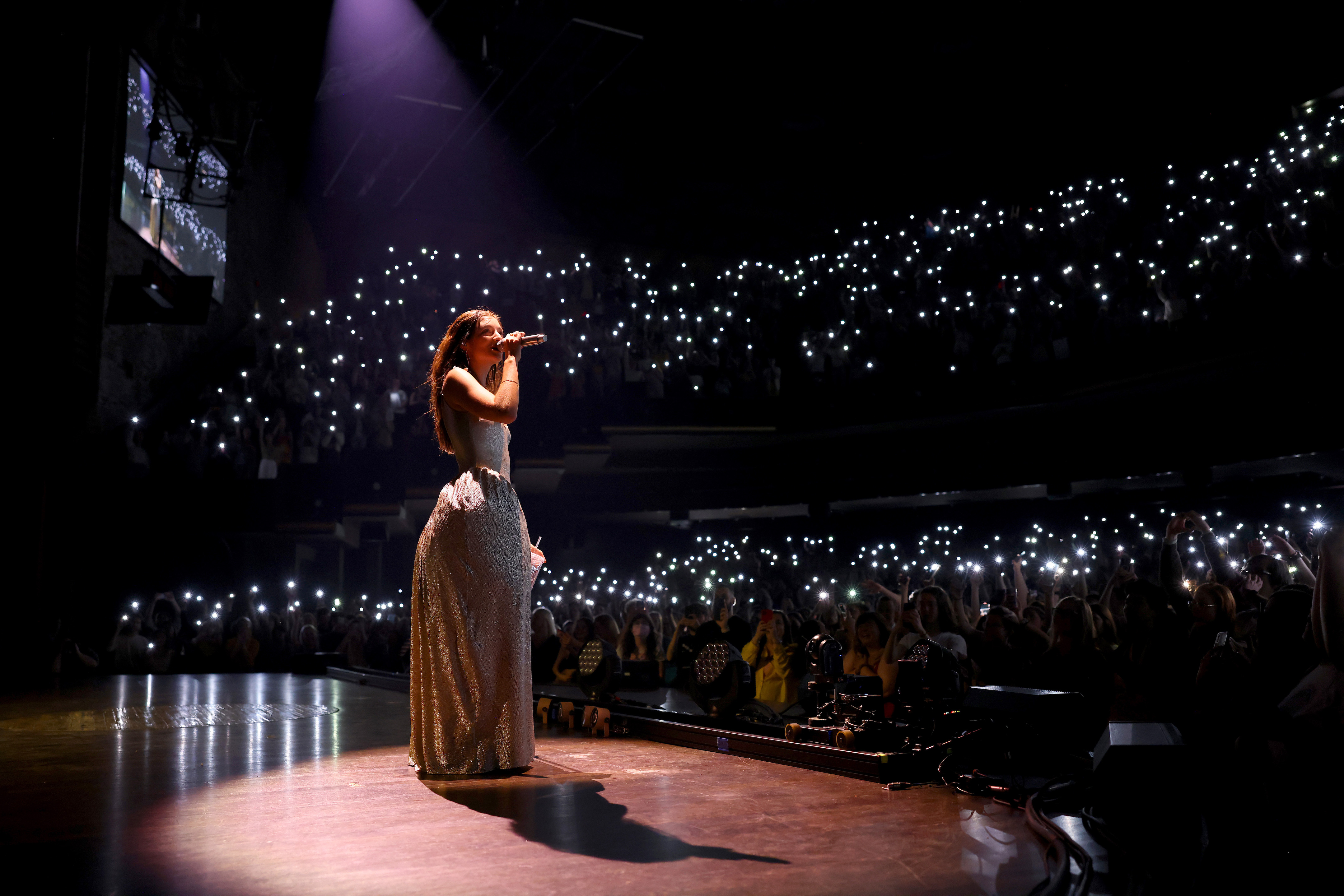 Lorde on stage in a dress with the audience holding up lights during opening night of her 'Lorde World Tour' at the Grand Ole Opry
