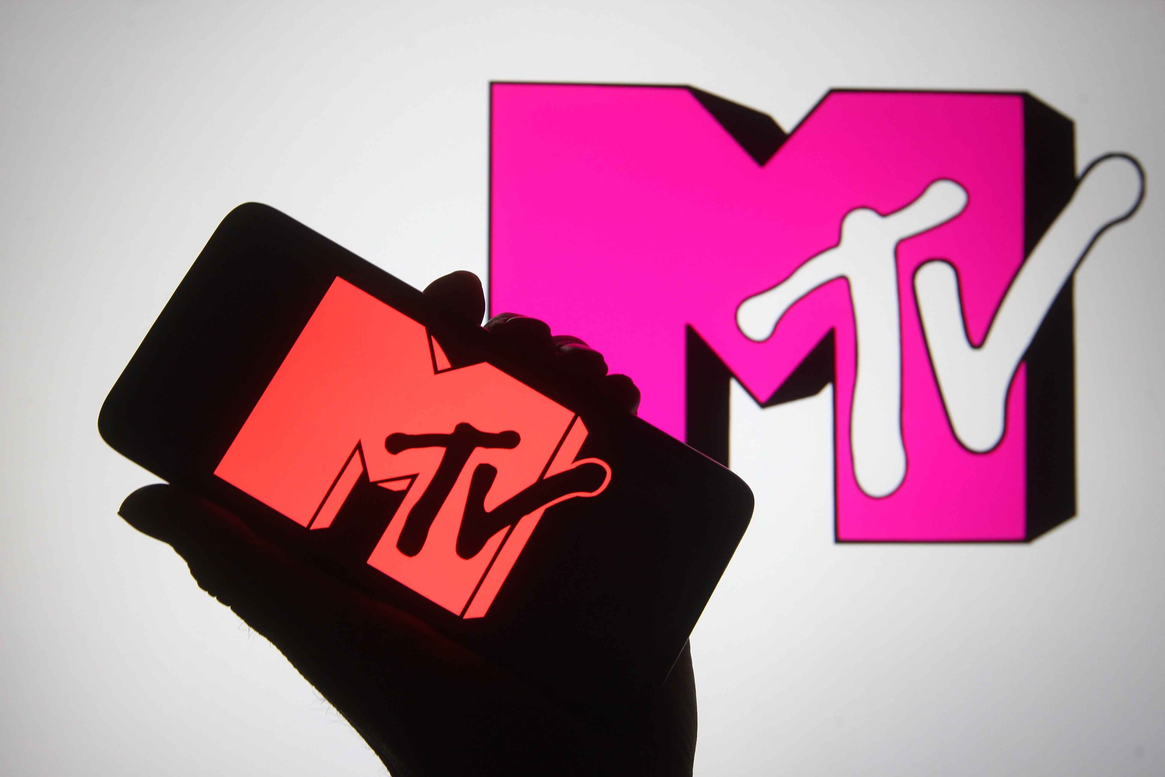 A silhouette hand holding a smartphone with MTV channel logo on its screen