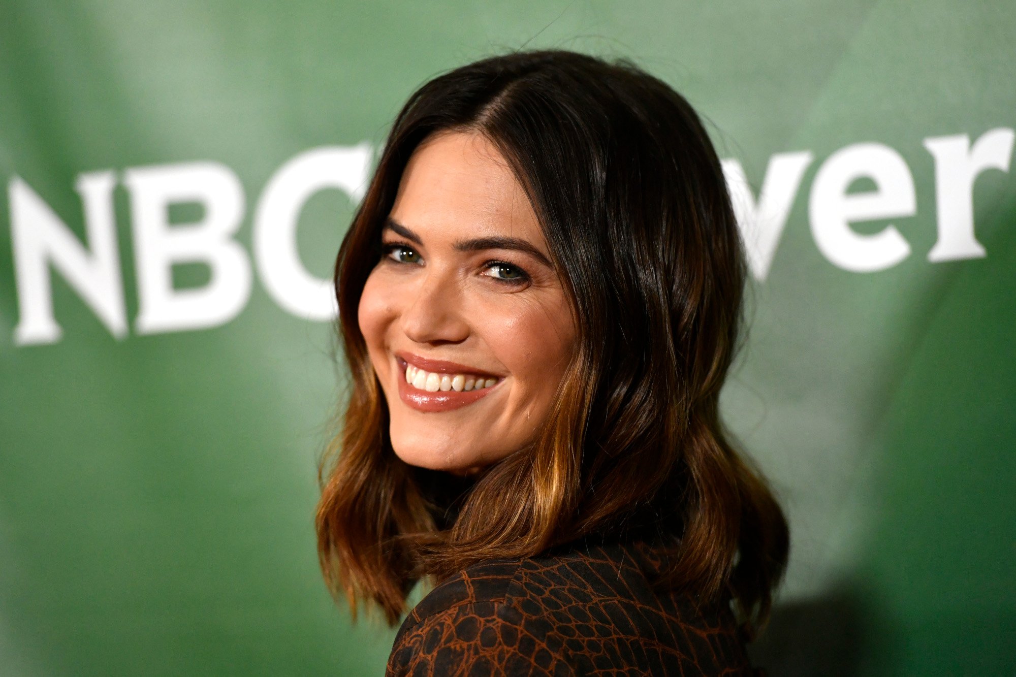 'This Is Us' star Mandy Moore, who commented on the finale scene between Rebecca and Jack. She's standing in front of a green wall with 'NBCUniversal' written on it, and she's wearing a brown sweater.