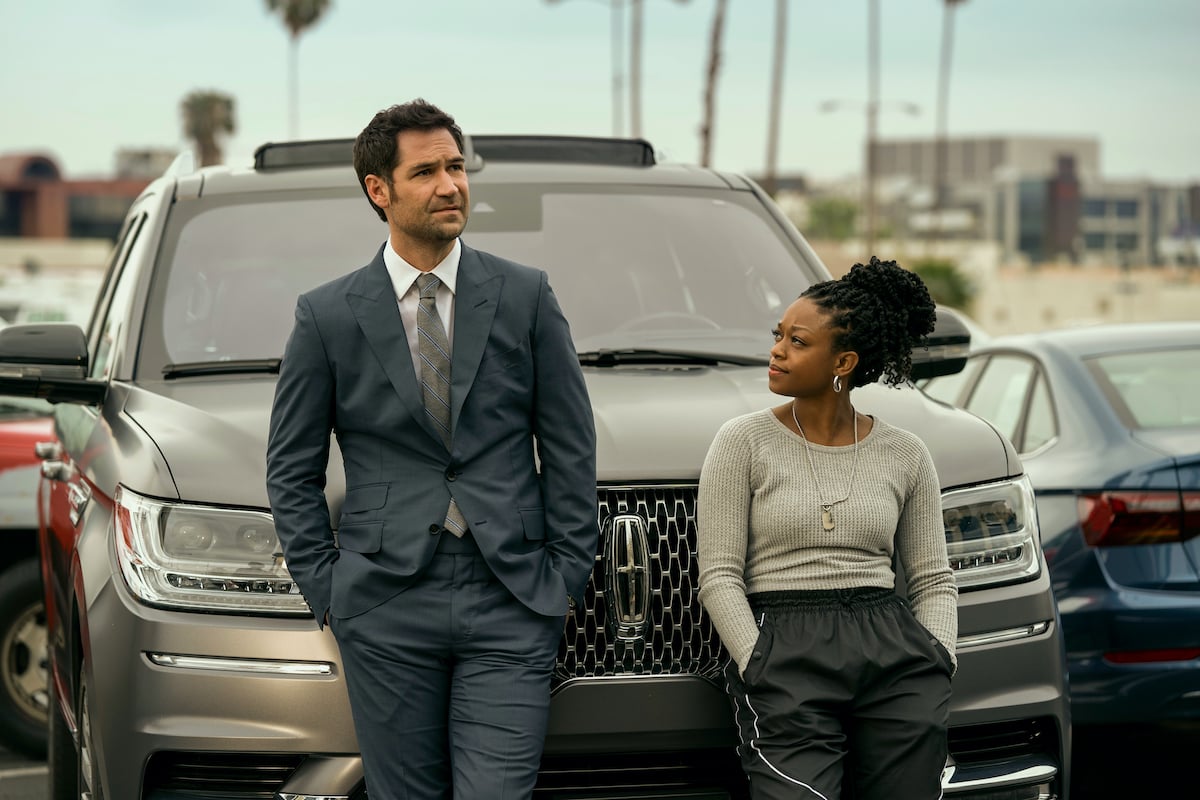 Manuel Garcia-Rulfo as Mickey Haller, Jazz Raycole as Izzy leaning against a Lincoln SUV in the Netfilx series 'The Lincoln Lawyer'