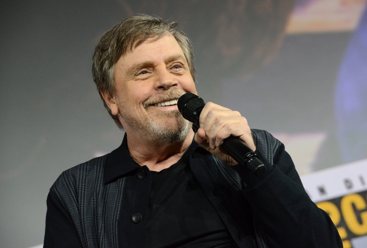 Mark Hamill smiling while holding a microphone.