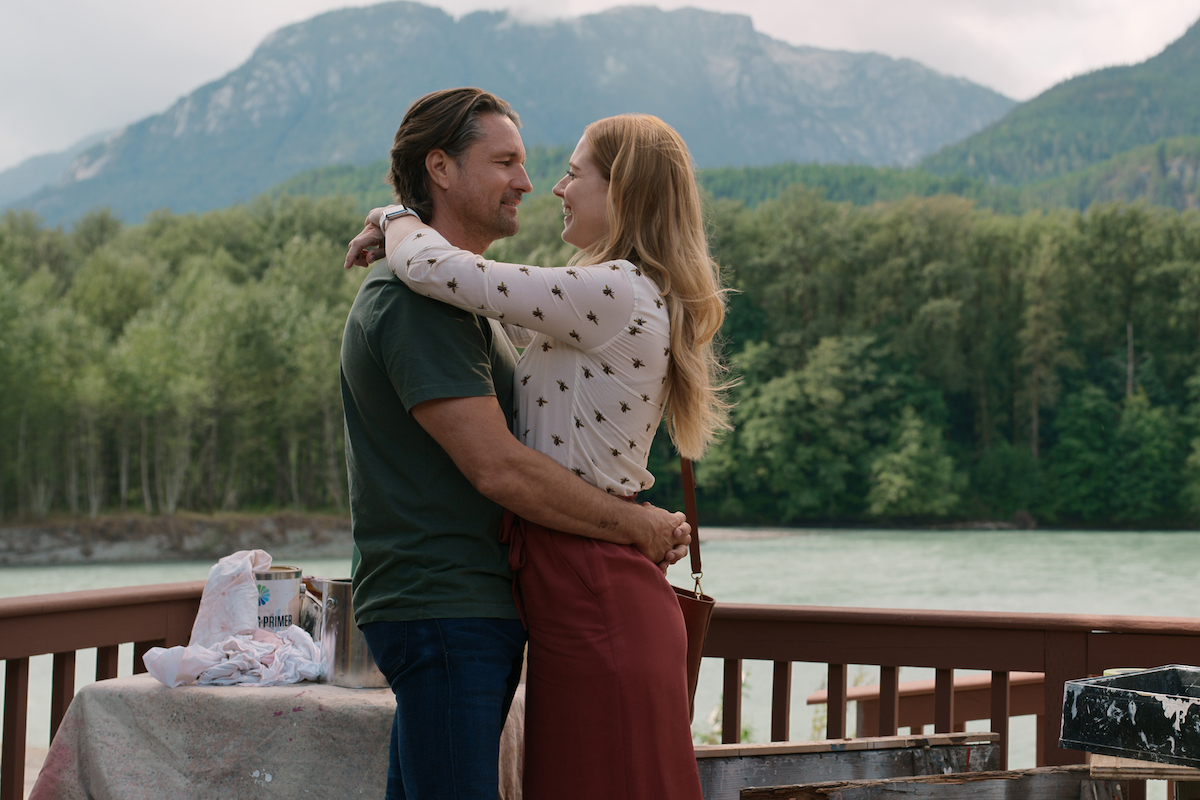 Martin Henderson as Jack Sheridan and Alexandra Breckenridge as Mel Monroe embracing on a deck overlooking the water and moutains 'Virgin River'
