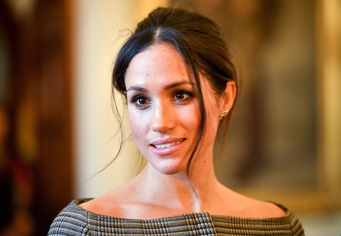 Meghan Markle looking on with her hair up and while wearing an off-shoulder outfit