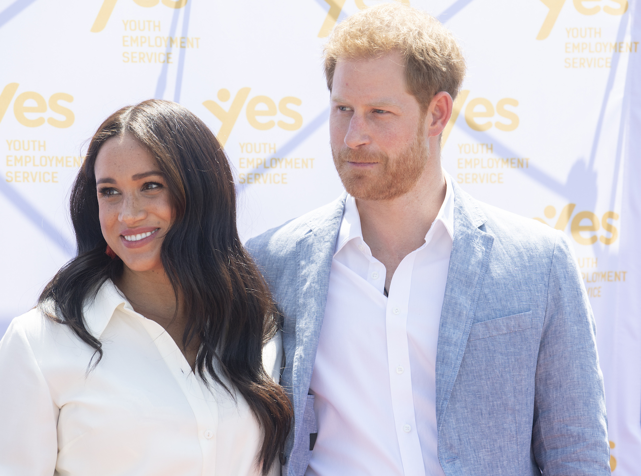 Meghan Markle wearing a white outfit and standing next to Prince Harry, who is wearing a gray jacket