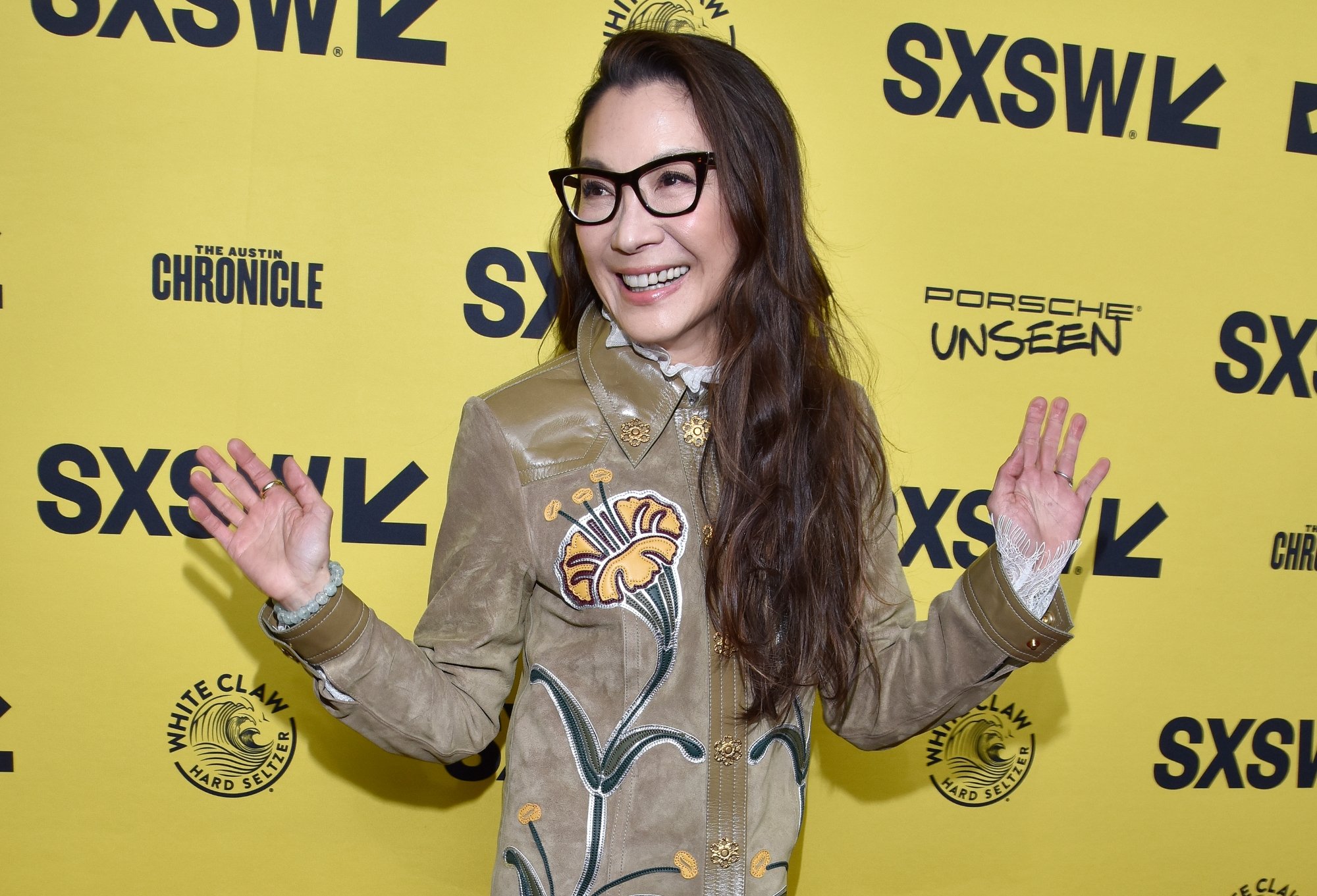 'Minions: The Rise of Gru' actor Michelle Yeoh standing in front of a yellow SXSW Film Festival step and repeat holding her hands out