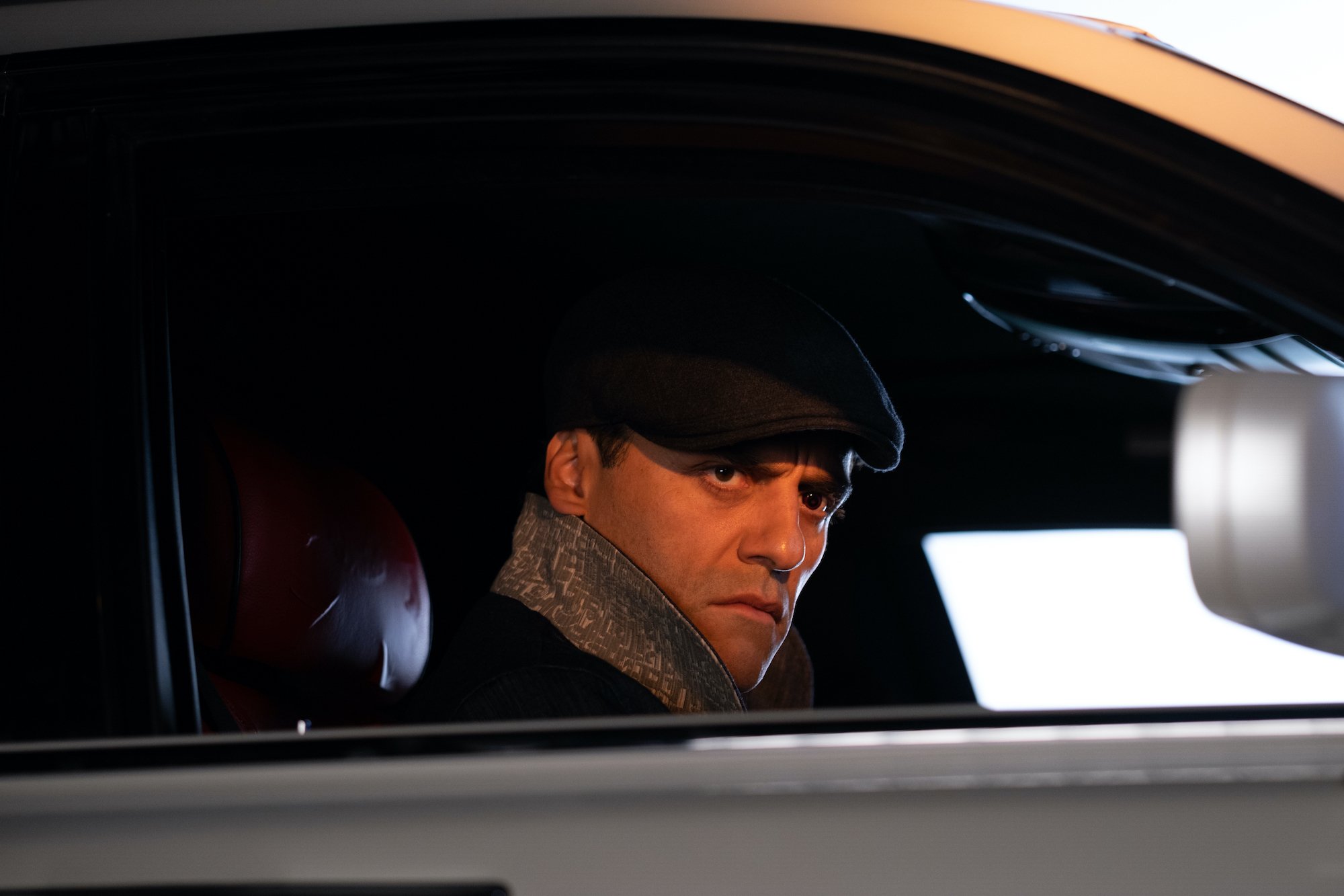 Oscar Isaac as Jake Lockley in the 'Moon Knight' finale on Disney+. He's sitting in a car and wearing a flat cap.