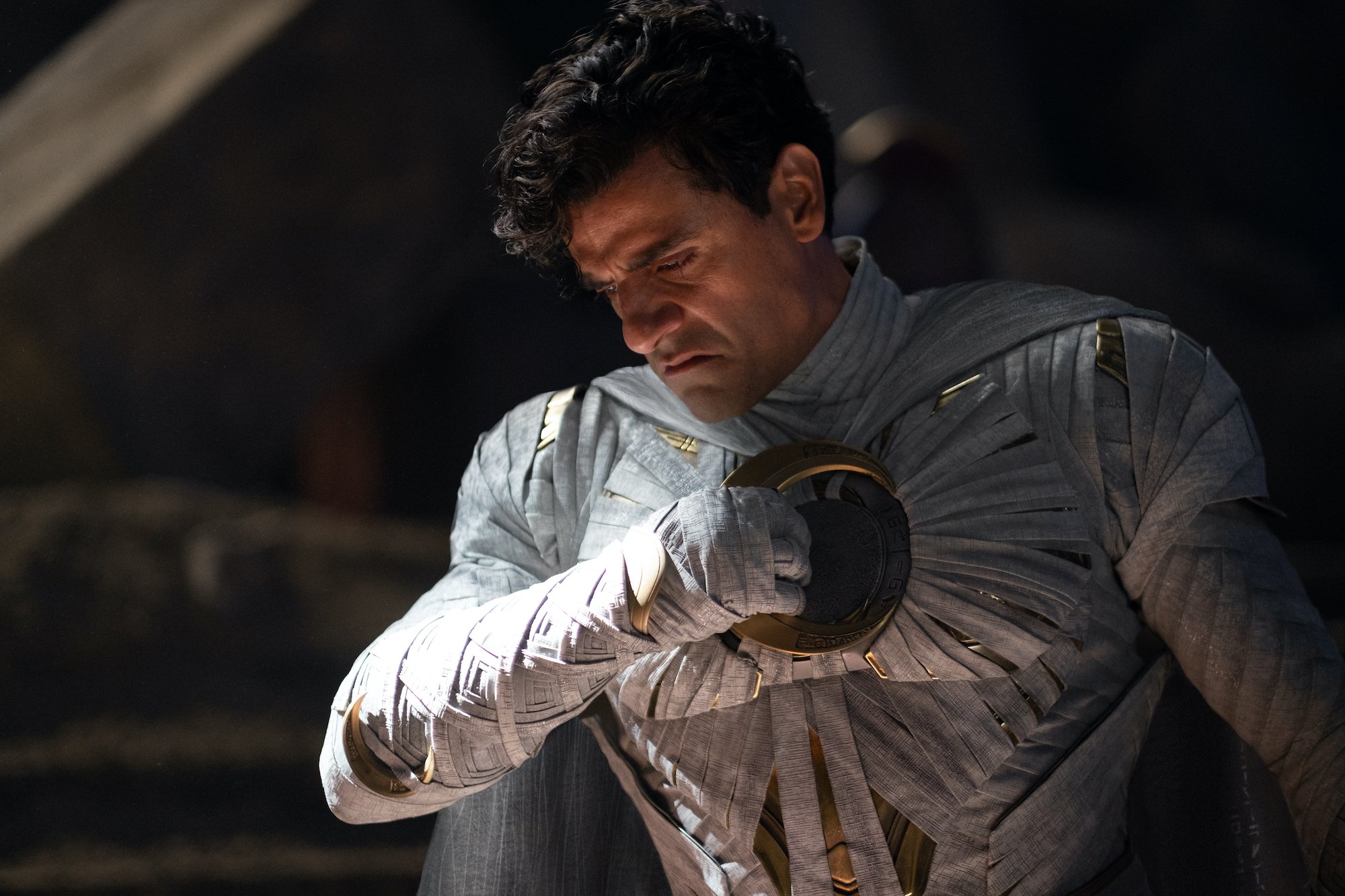 Oscar Isaac as 'Moon Knight' lead Marc Spector, who survived the Blip. He's wearing the light grey Moon Knight costume, but his mask is off. He's holding a first to his heart.