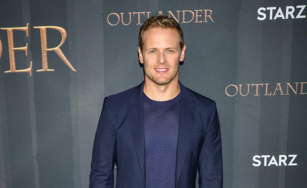 Outlander Sam Heughan wearing a blue suit and smiling for the cameras arrives at the Season 6 Premiere at The Wolf Theater at the Television Academy on March 09, 2022 in North Hollywood, California