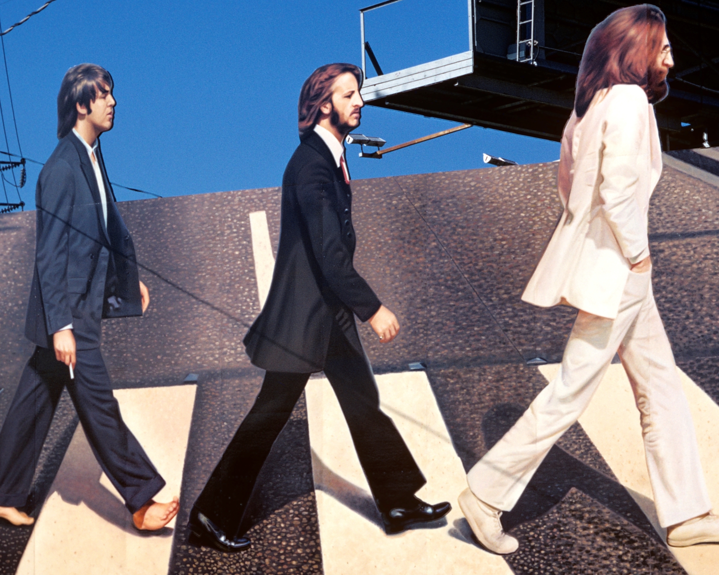 Paul McCartney, Ringo Starr, and John Lennon in a billboard based on the cover of The Beatles' 'Abbey Road'