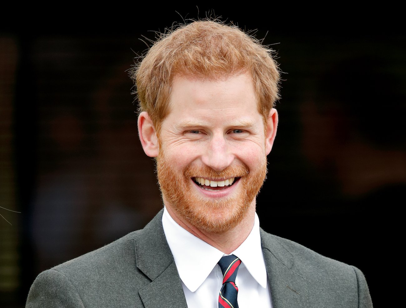 Prince Harry wearing a suit and grinning while looking toward the camera