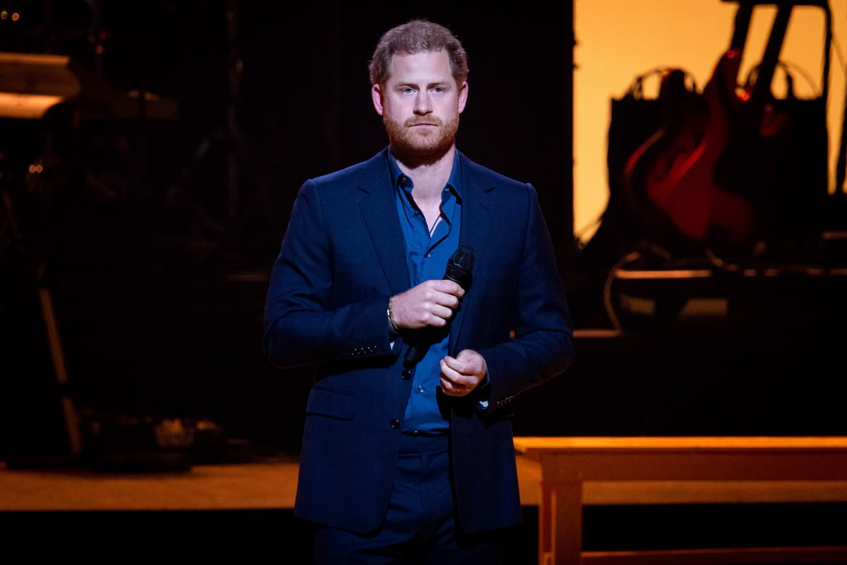 Prince Harry, whose memoir may be delayed to include Queen Elizabeth's Platinum Jubilee, stands onstage holding a microphone