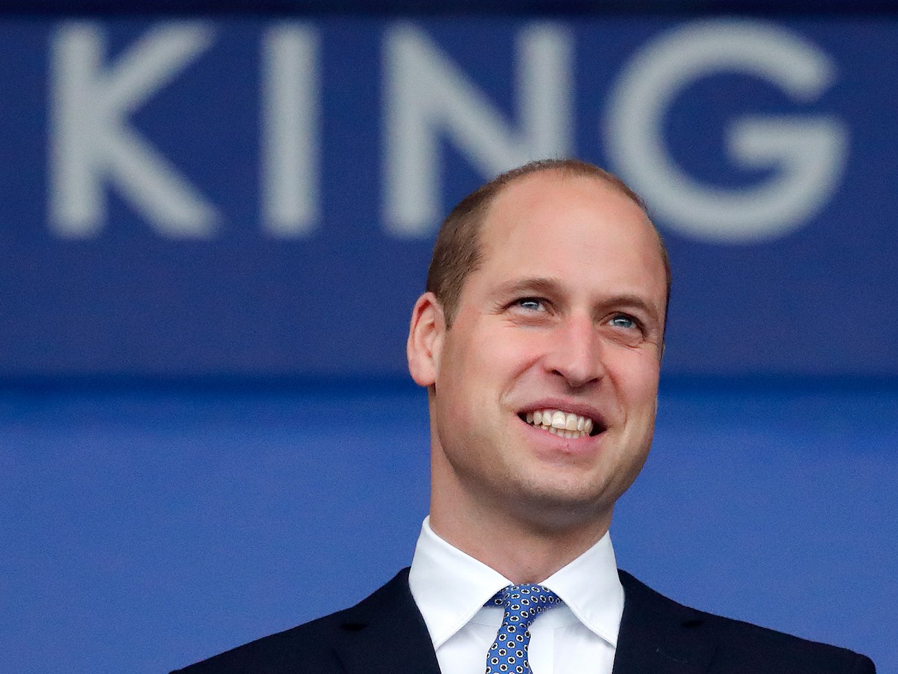 Prince William wearing a suit and smiling, seen from below